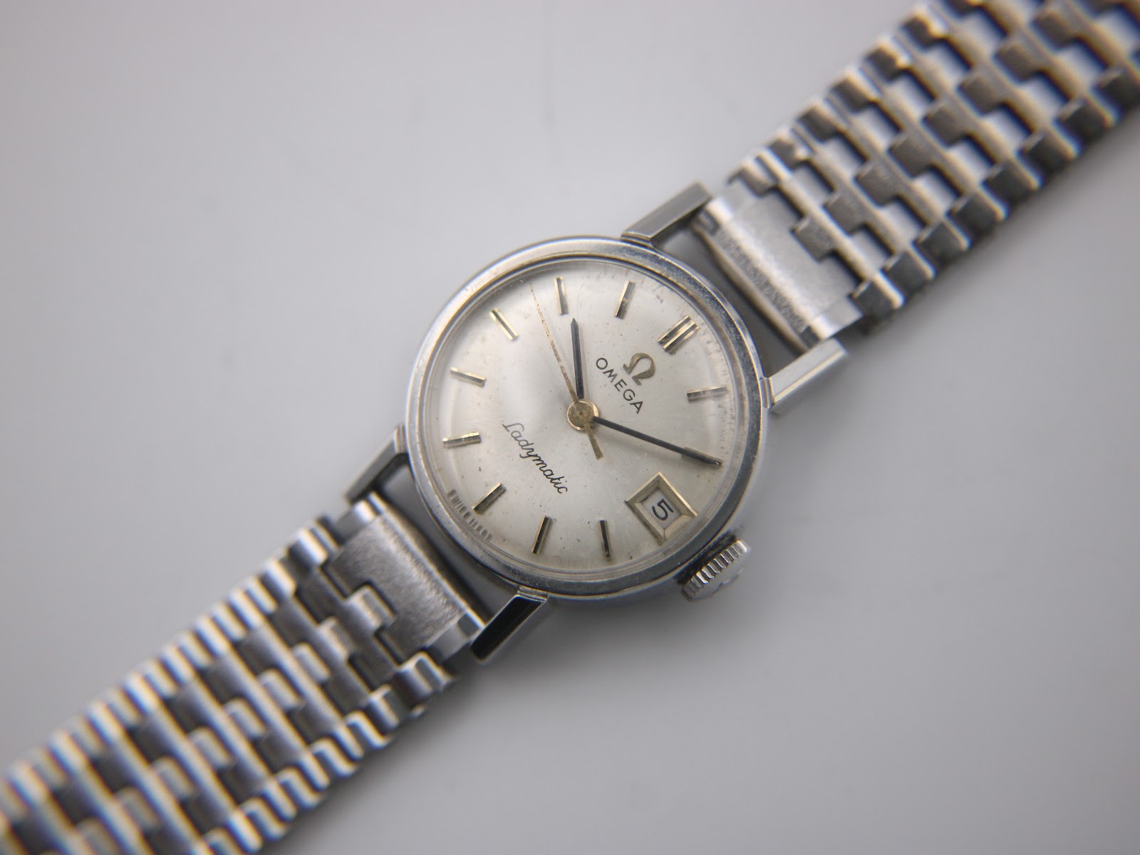 Close-up of the Omega Ladymatic's cream dial, showing applied baton indices, Omega logo, Ladymatic script, and date window.