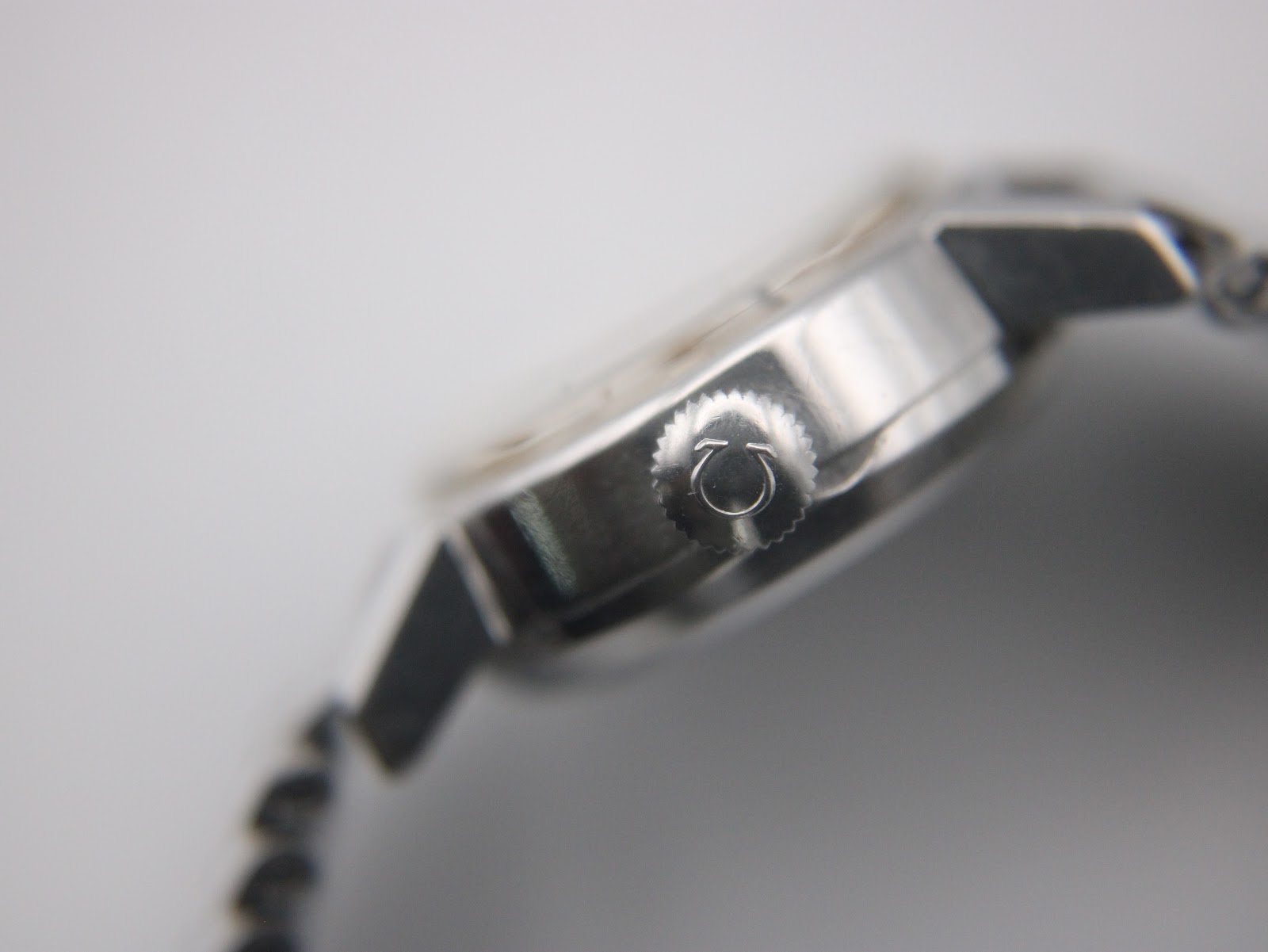 Extreme close-up of the watch's side, featuring the Omega-signed crown with the Greek letter Omega symbol.