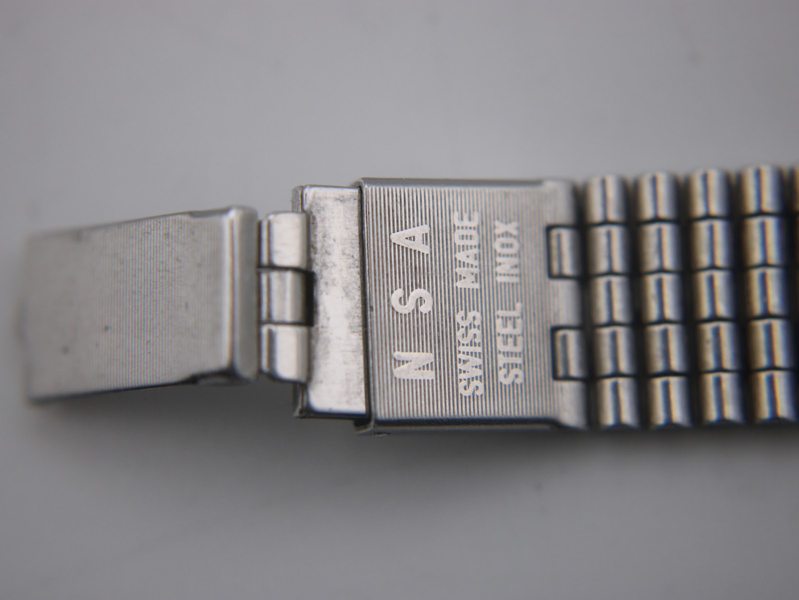 Detailed view of the watch bracelet's clasp, revealing the 'SWISS MADE INOX ACIER UNSA' engravings.
