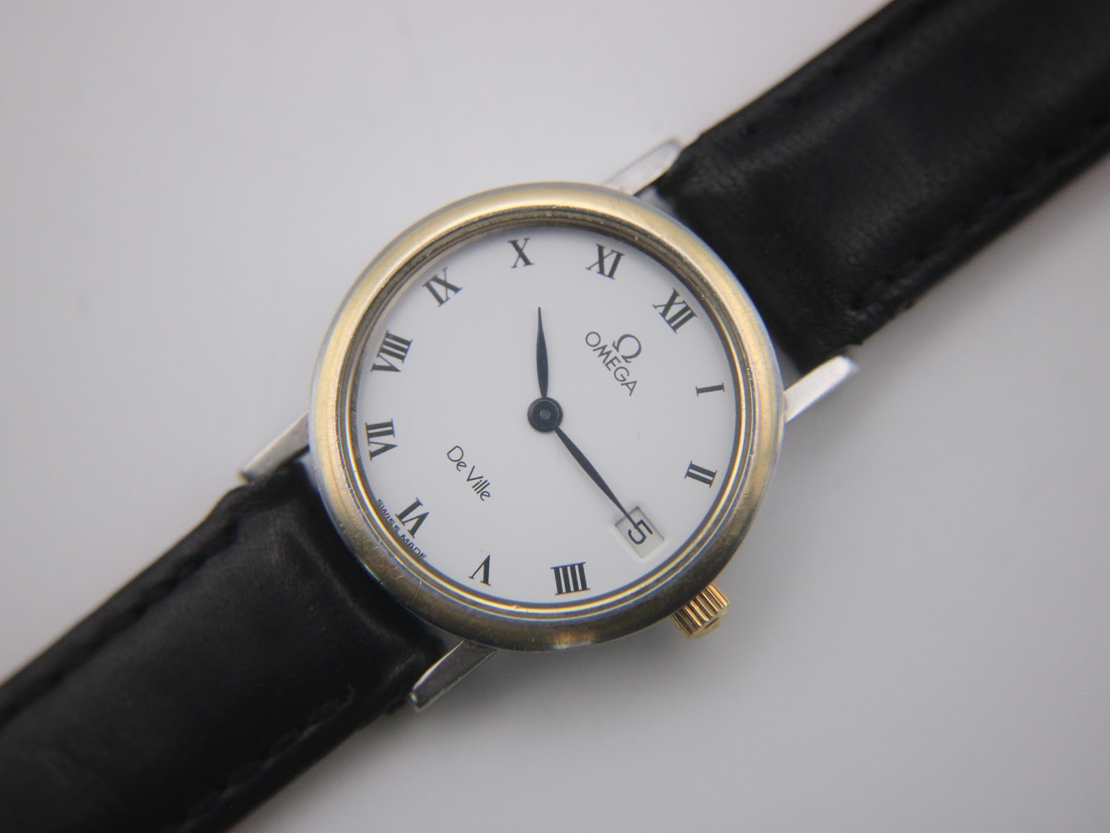 Alternative angled side view of the Omega De Ville watch on a stand, highlighting the two-tone case.