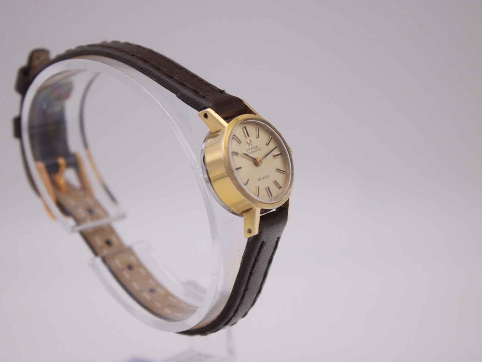 Another side profile view of the Omega De Ville watch on a stand, showing the curved lugs and strap attachment.
