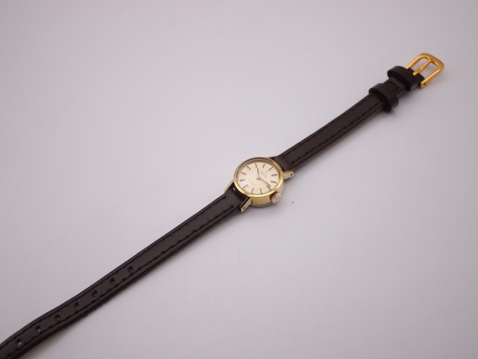 Overhead view of the Omega De Ville watch with its brown leather strap extended, showing the small case size.