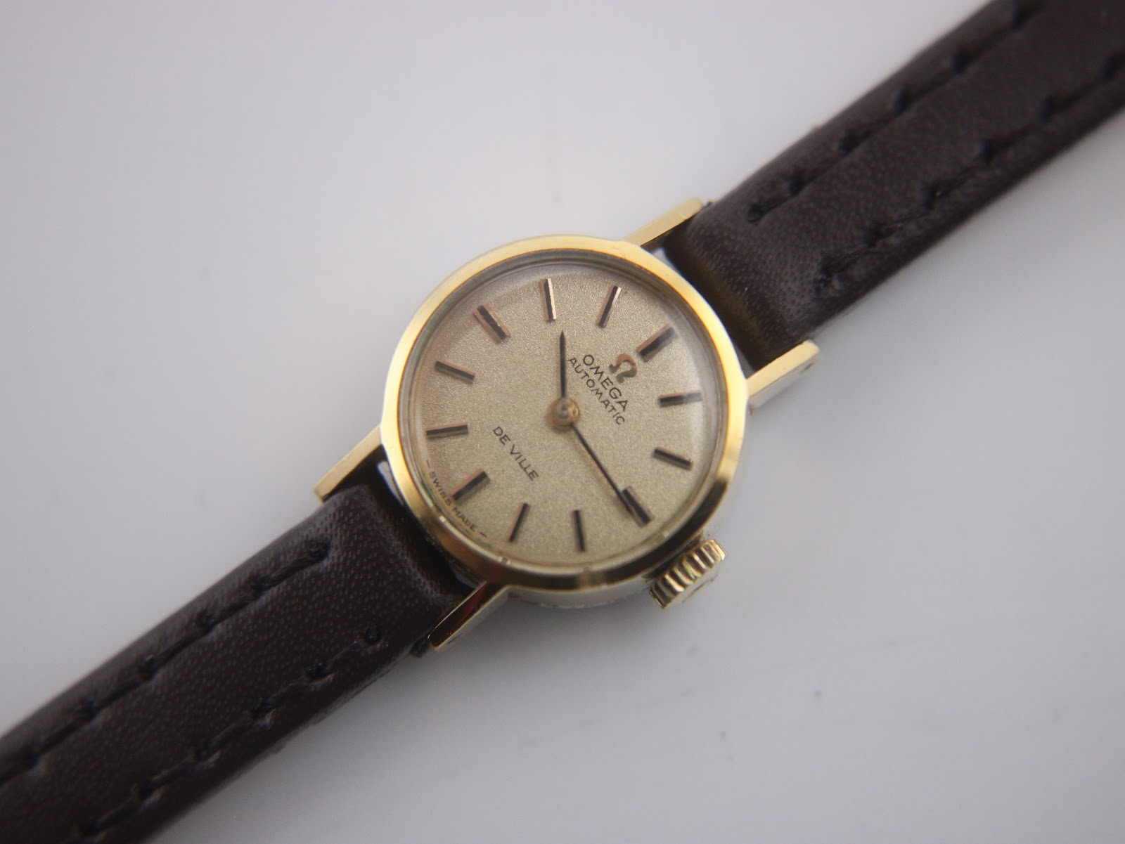 Close-up front view of the Omega De Ville dial, revealing the champagne colour, baton indices, and 'Omega Automatic De Ville' text.
