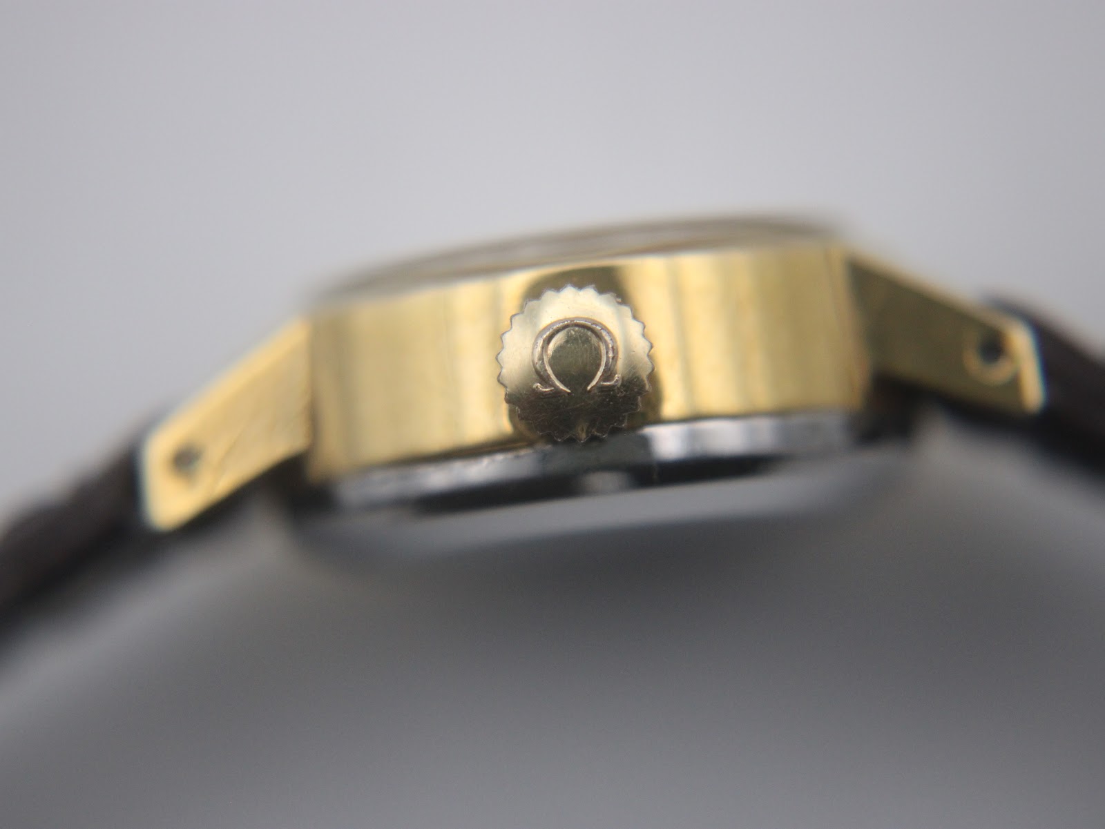 Close-up side view of the Omega De Ville crown, signed with the iconic Omega logo.