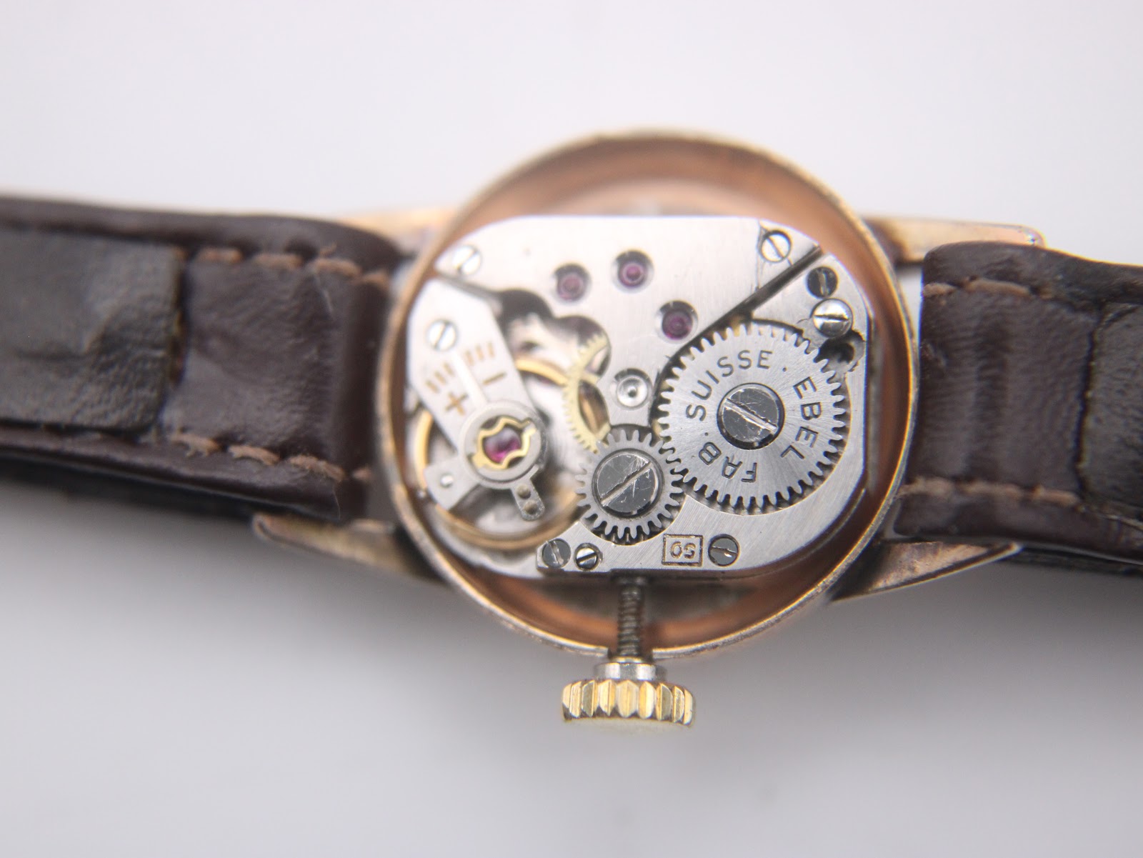 Macro shot of the EBEL manual wind movement with visible gears and 'EBEL SUISSE FAB.' engraving.