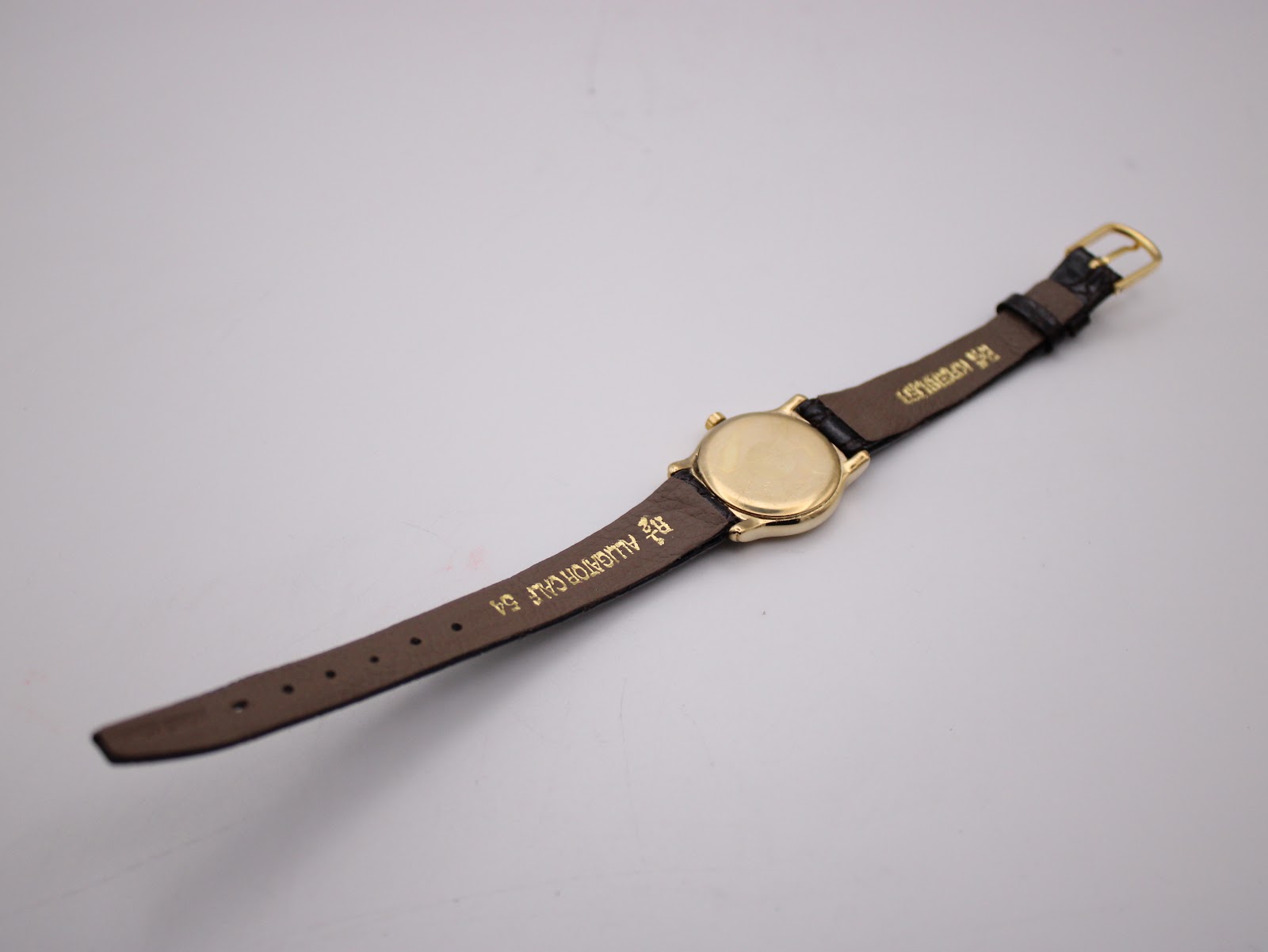 Back view of the Raymond Weil watch showing the plain gold case back and the underside of the black leather strap with markings.
