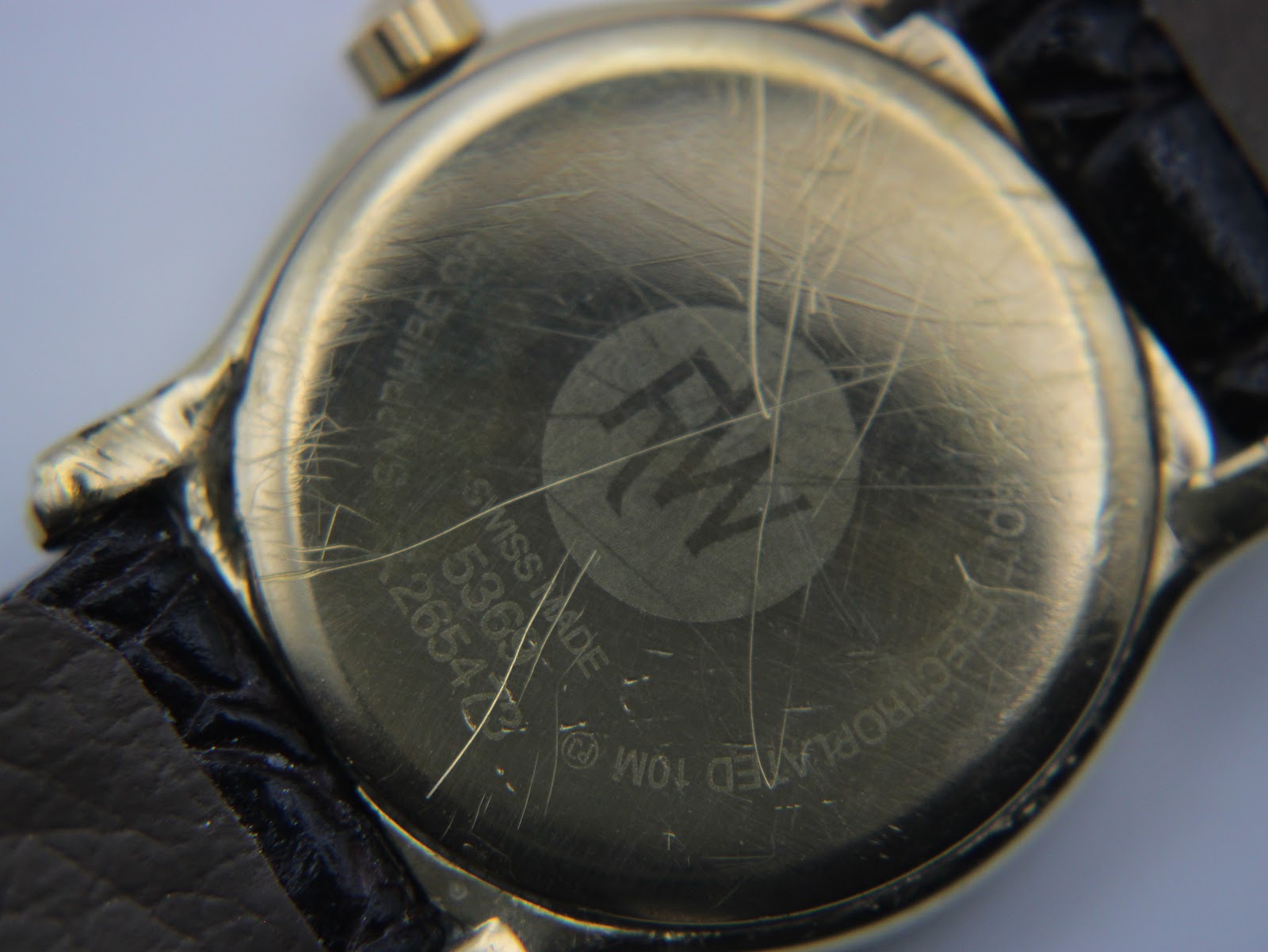 Close-up of the Raymond Weil watch case back, showing surface scratches and engraved model 5360, serial 26543, sapphire crystal, electroplated 10m.