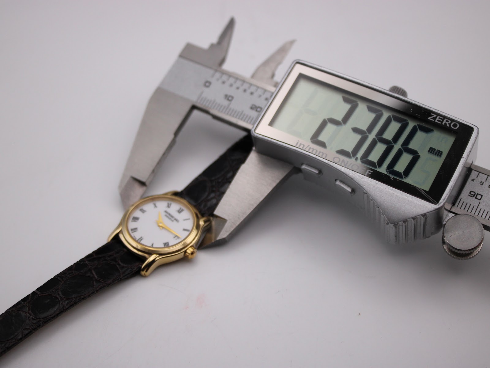 Digital caliper measuring the Raymond Weil watch case diameter, showing a precise reading of 23.86mm.