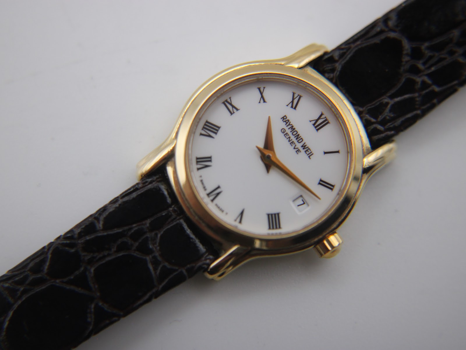 Close-up of the Raymond Weil watch dial, showing the roman numerals, gold hands, date window, and 'swiss made' text.
