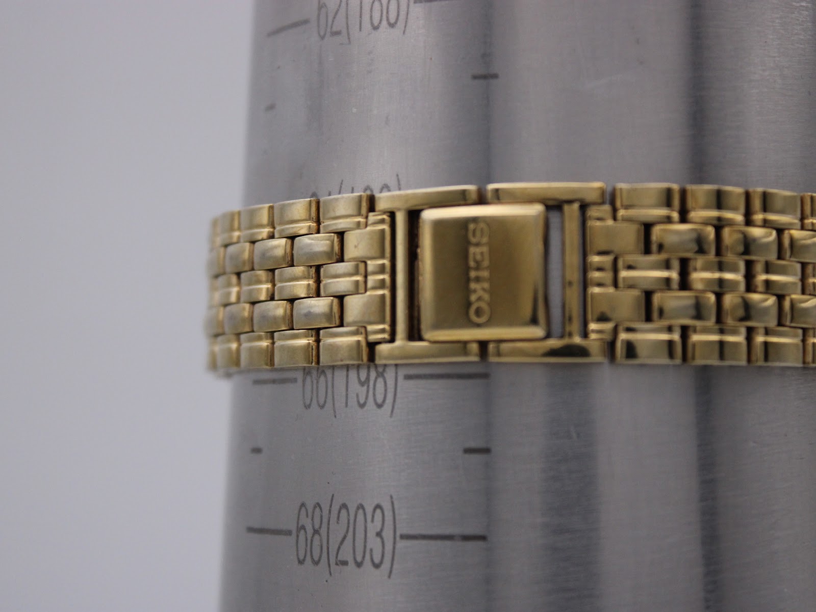 Close-up of the Seiko watch's gold-tone integrated bracelet and "SEIKO" signed clasp on a wrist sizing gauge, showing a wrist circumference of approximately 18.5cm.