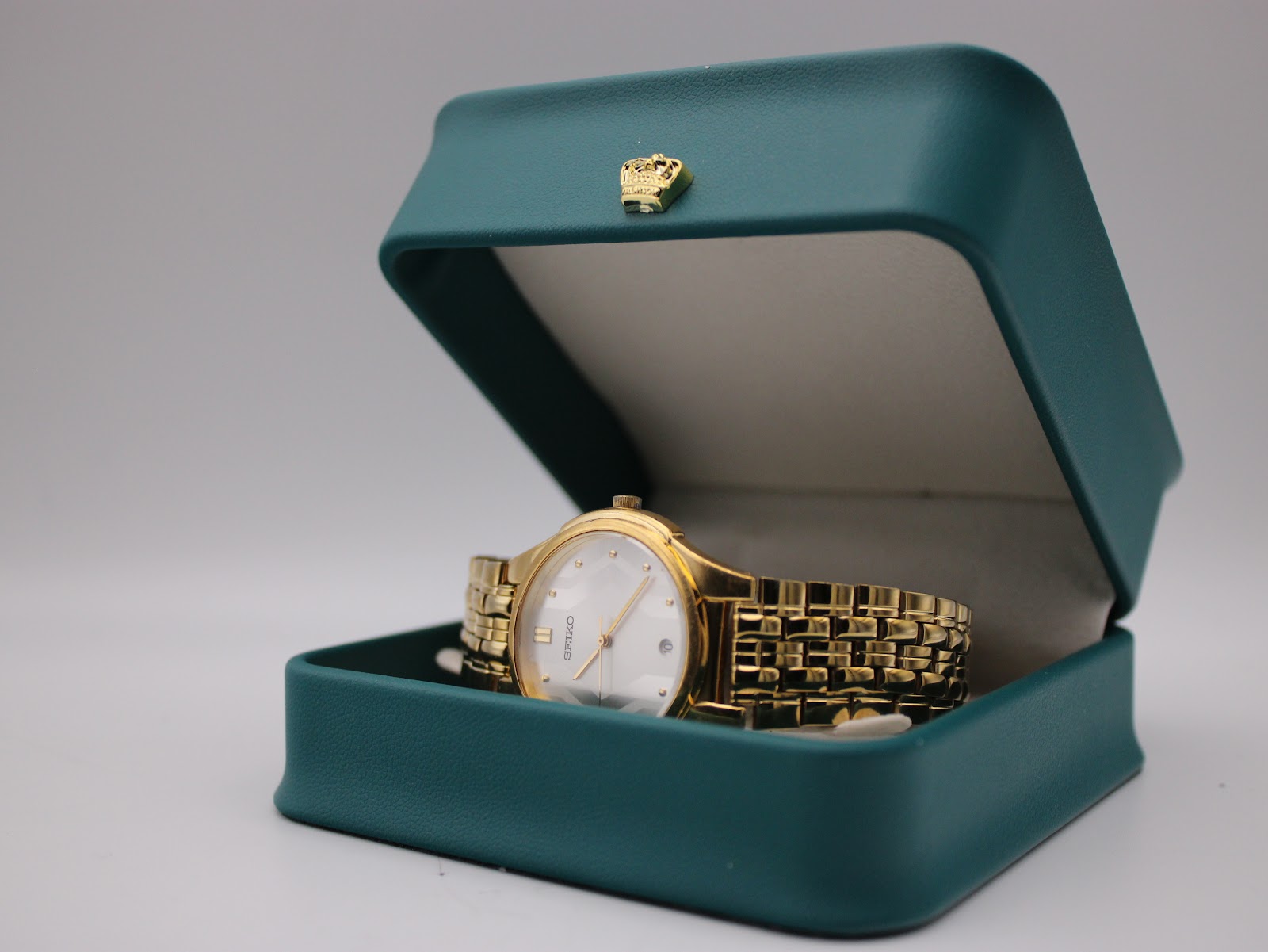 The Seiko gold-tone watch resting inside its original teal presentation box with a gold crown emblem.
