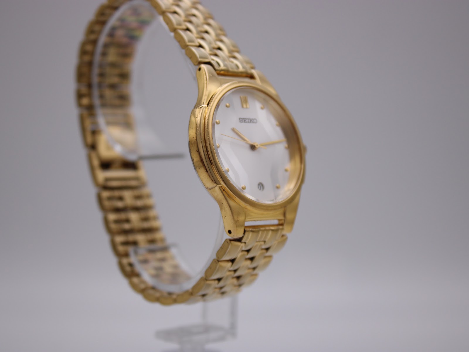 Another angled side view of the Seiko watch on a clear stand, showing the curvature of the case and bracelet links.