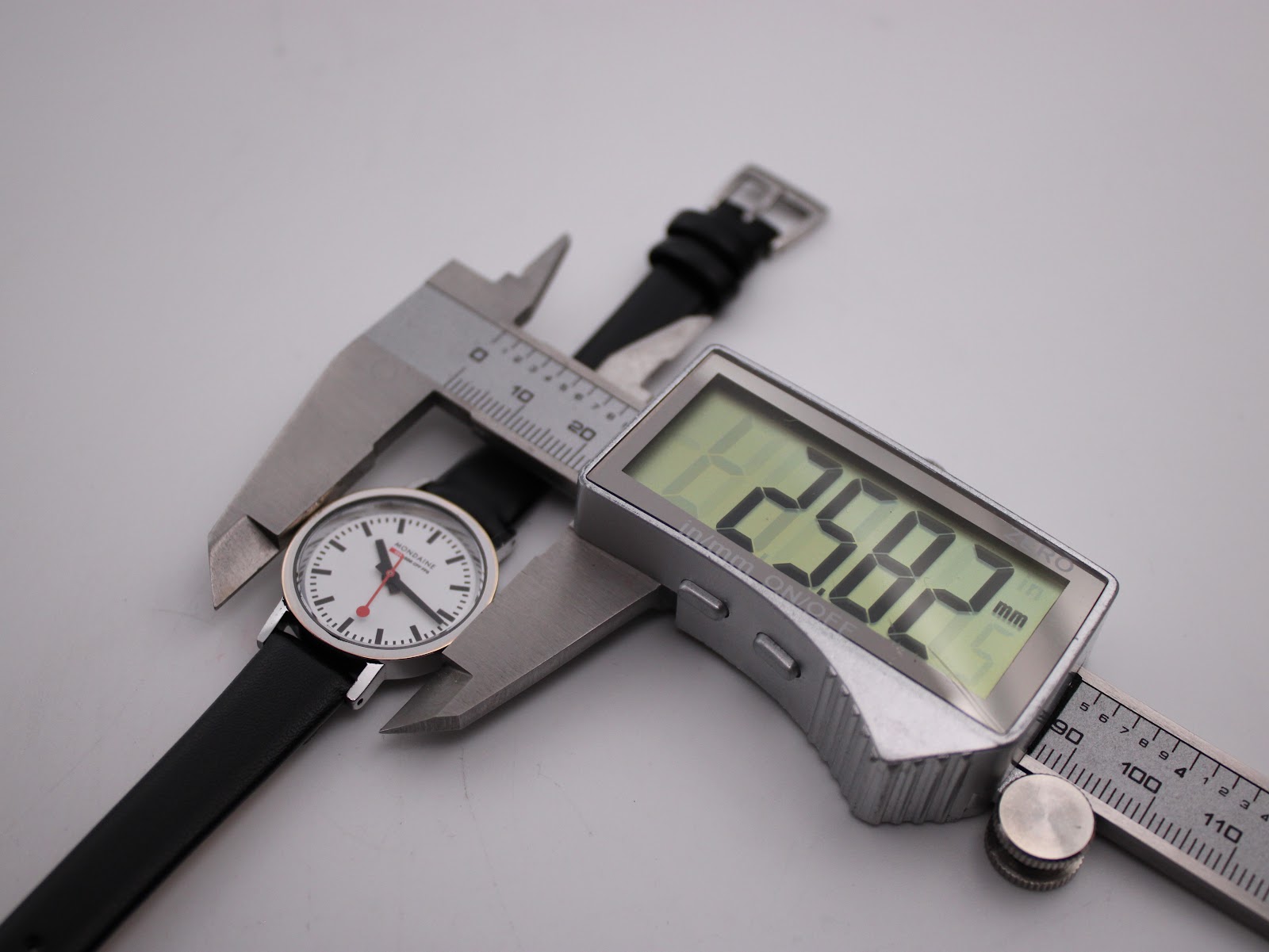 Top-down view of the Mondaine watch being measured by a digital caliper, displaying a case size of 29.82mm.