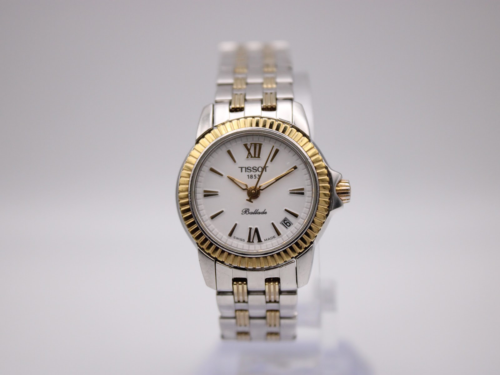 Front view of Tissot Ballade ladies' two-tone watch with white dial and gold-tone Roman numerals on a display stand.