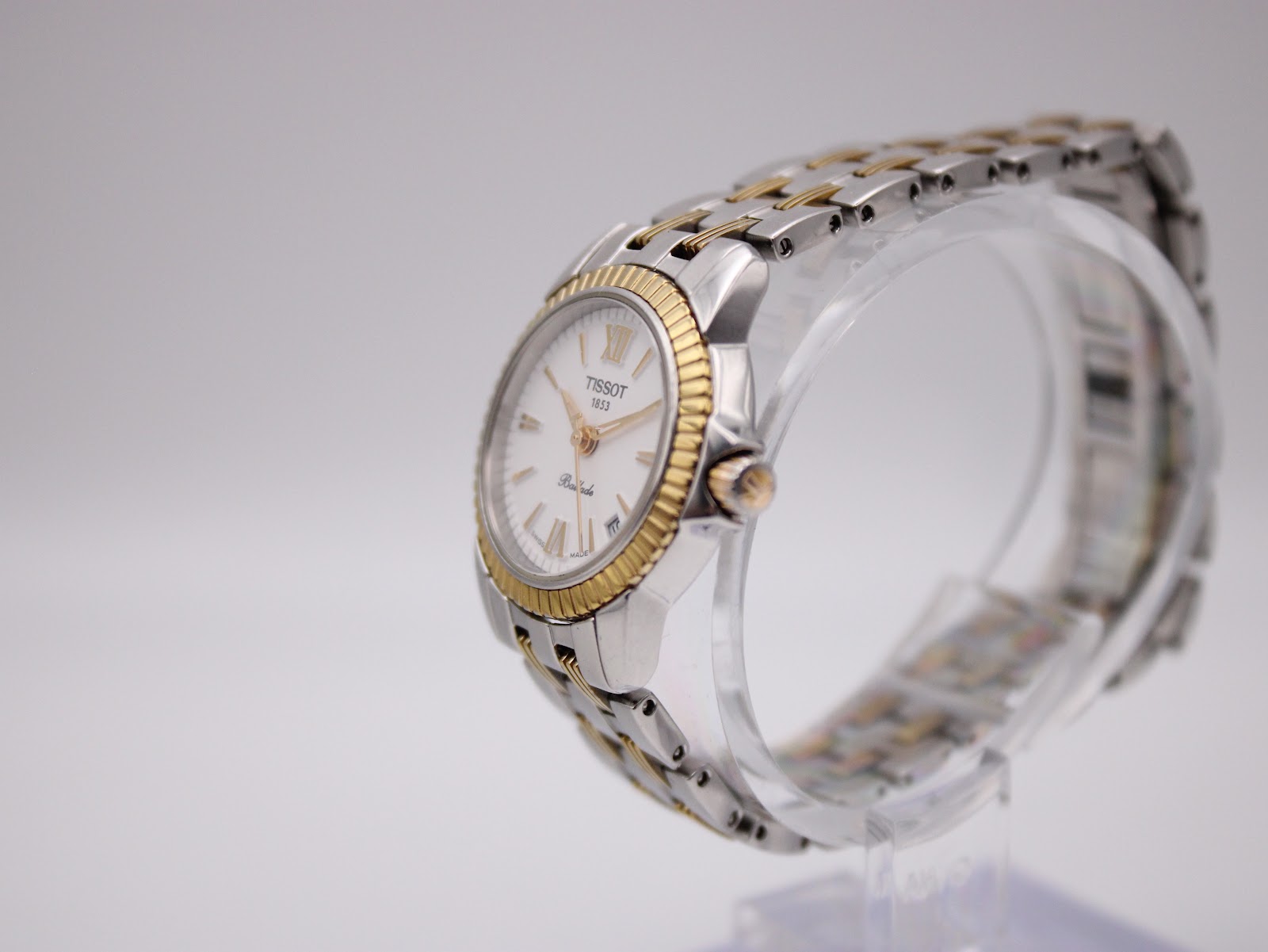 Angled side view of the Tissot Ballade watch on a stand, showcasing the fluted gold PVD bezel and two-tone bracelet.