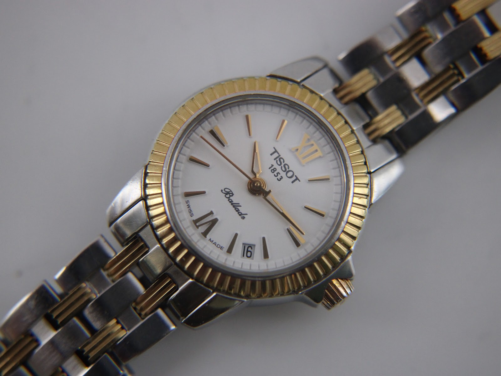 Close-up top-down view of the Tissot Ballade's white dial, featuring gold-tone hands, Roman numerals, and a date window.