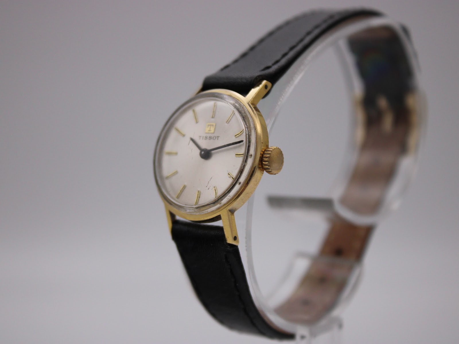 Angled side view of the Tissot watch, highlighting the gold case and profile on a display stand.