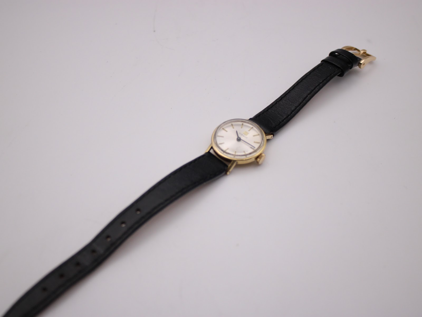Overhead view of the Tissot watch with the black leather strap laid out flat, showing its full length.