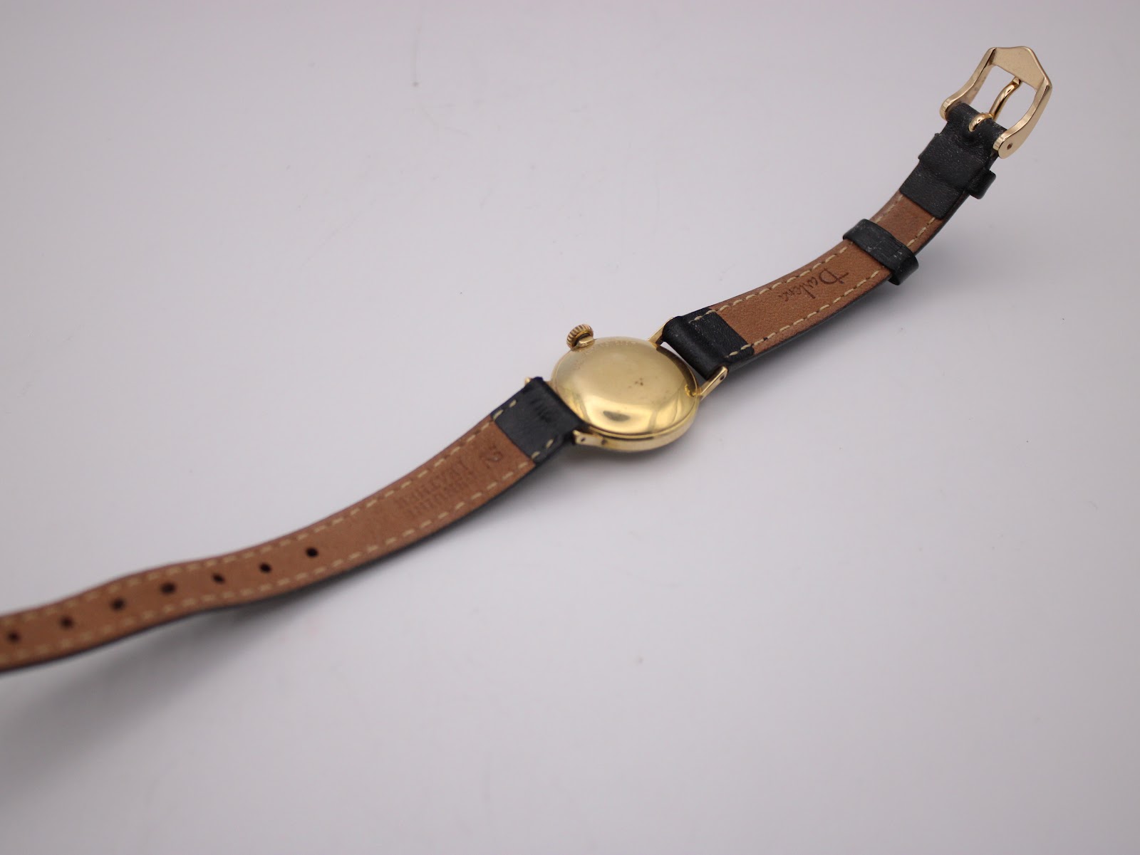 Rear view of the Tissot watch with the strap laid flat, showing the gold-tone case back and the brown underside of the leather strap.