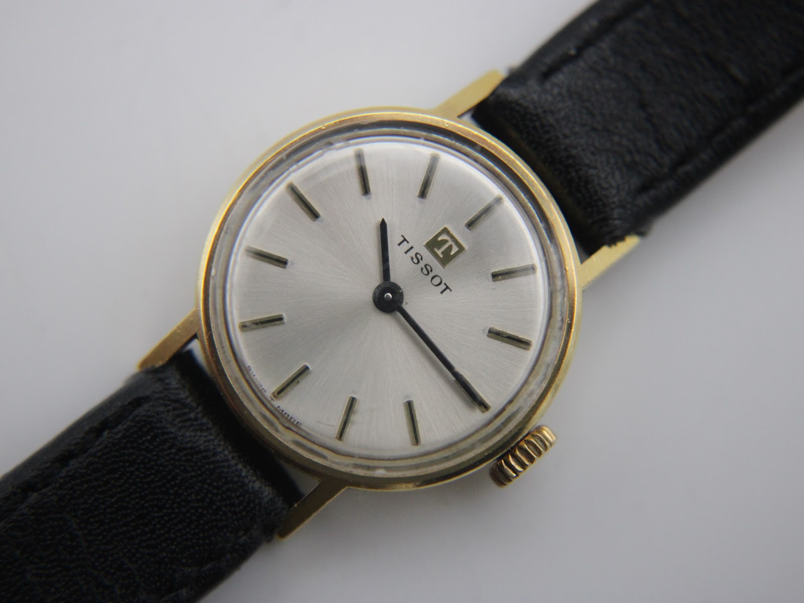 Close-up front view of the Tissot watch dial, revealing the Tissot logo, applied baton indices, and sunburst silver finish.