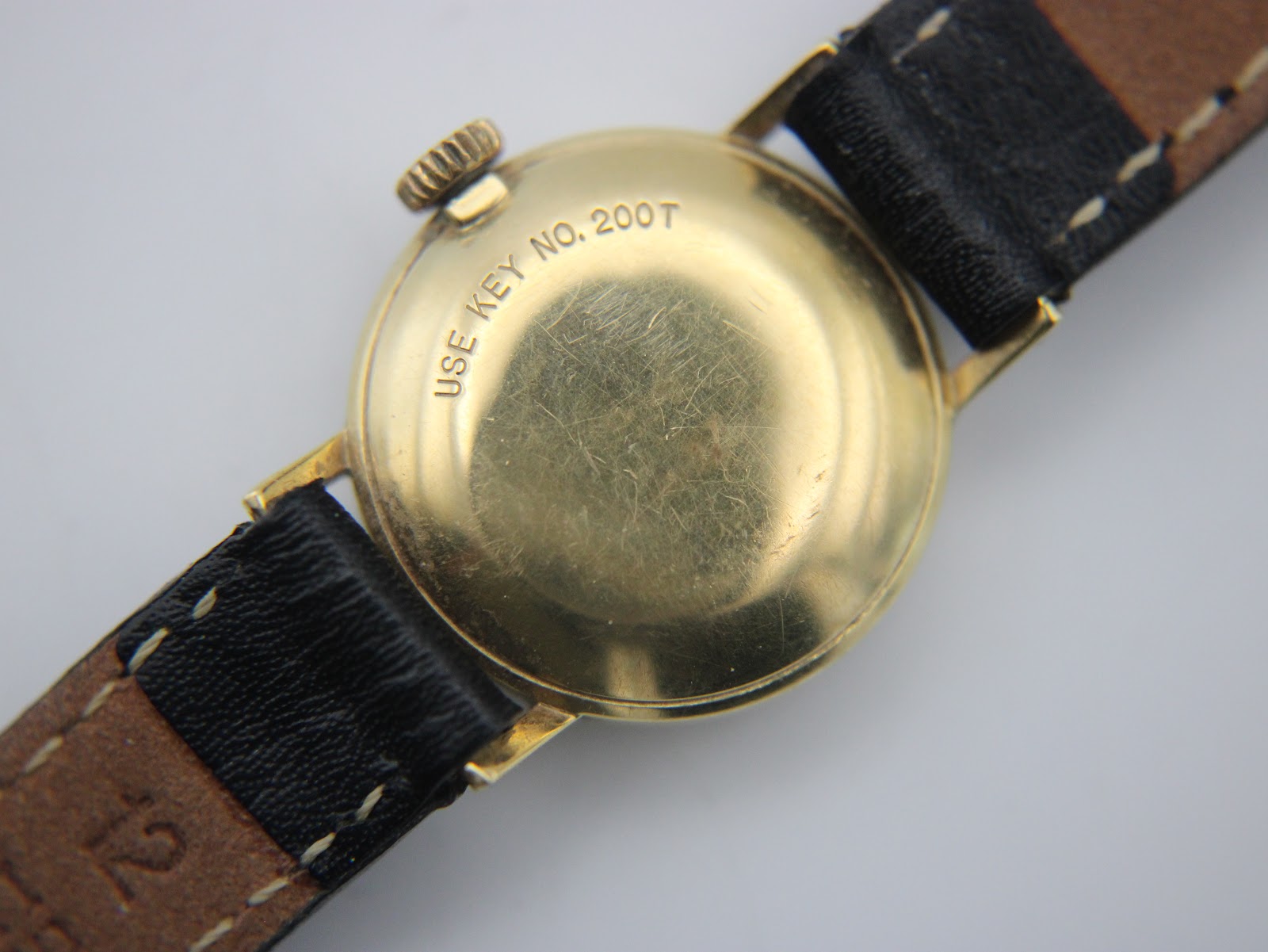 Close-up of the gold-tone case back of the Tissot watch, showing 'USE KEY NO. 200T' engraving and surface scratches.