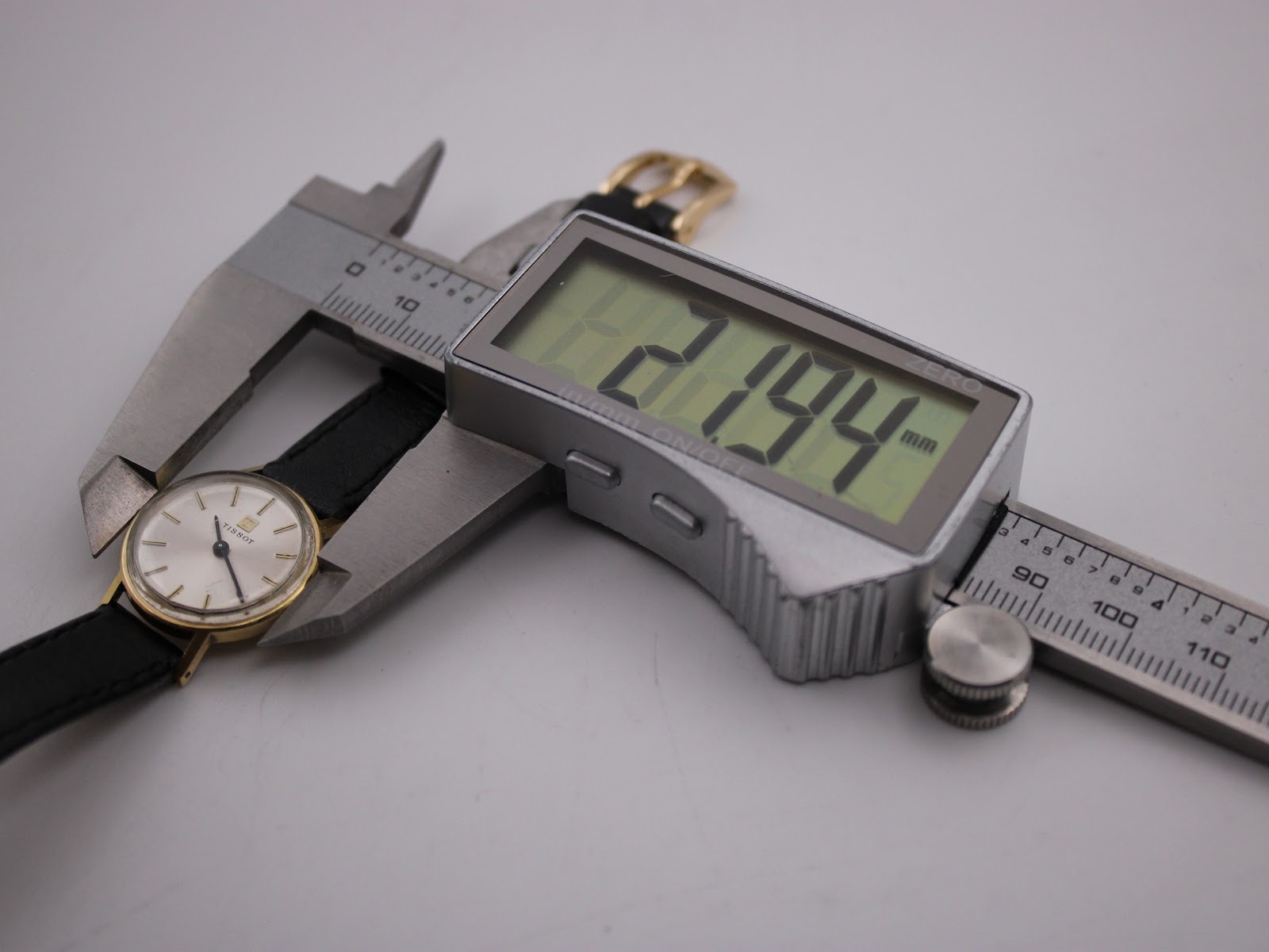 Side view of the Tissot watch being measured by a digital caliper, displaying a precise case diameter of 21.94mm.