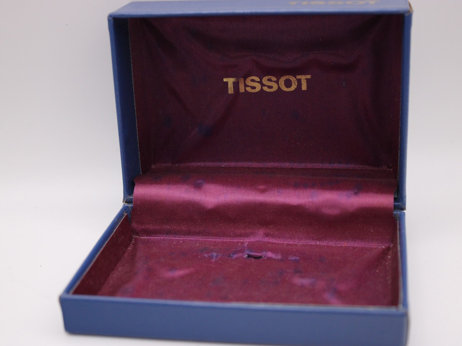 Open original Tissot watch box, showing the dark blue exterior and purple satin interior with the gold Tissot logo.