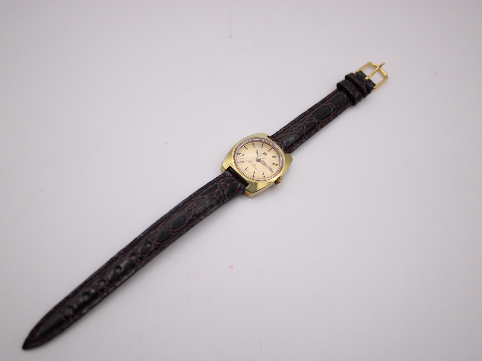 Overhead view of the Tissot watch with its full length brown crocodile-effect leather strap laid flat.