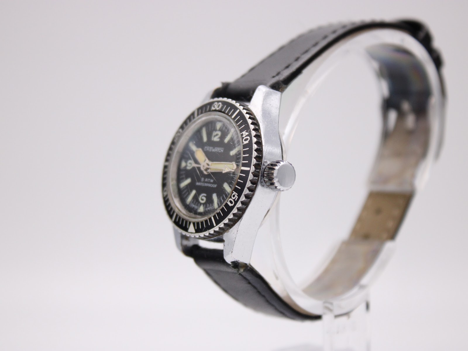 Angled side view of the CASWATCH watch, highlighting the silver case, rotating black bezel, and crown.