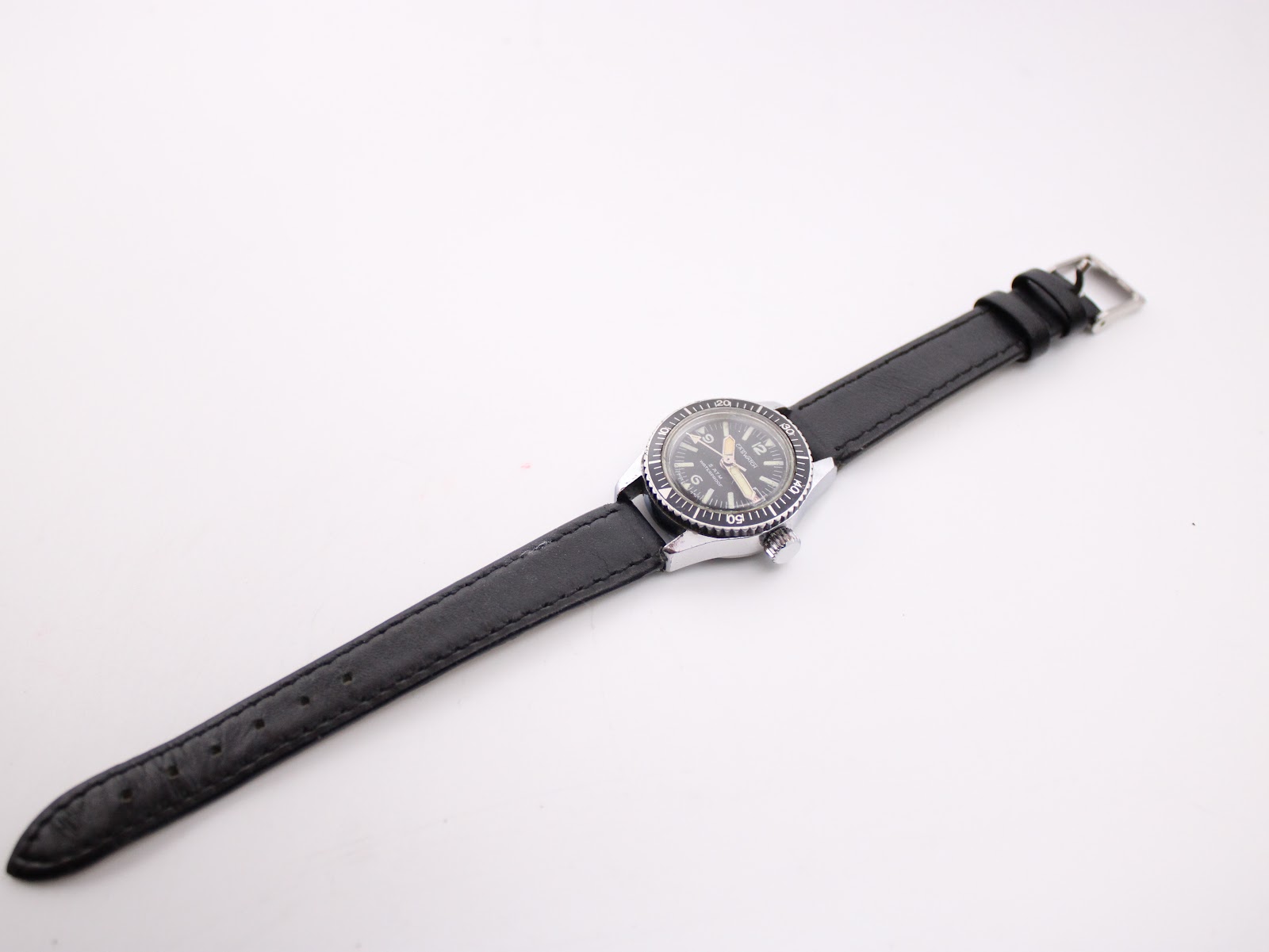 Overhead view of the CASWATCH watch with its black leather strap fully extended on a white background.