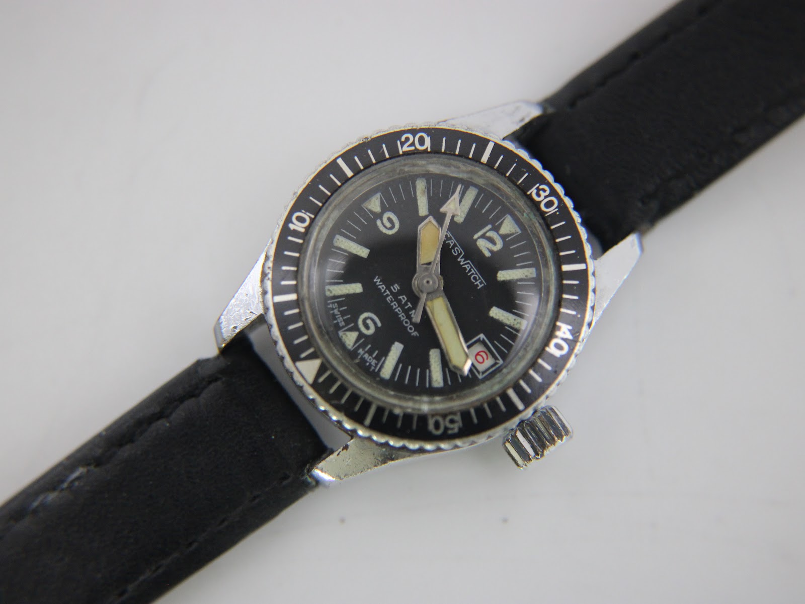 Close-up front view of the CASWATCH black dial, showing the date window, luminous hands, and "5 ATM WATERPROOF" text.