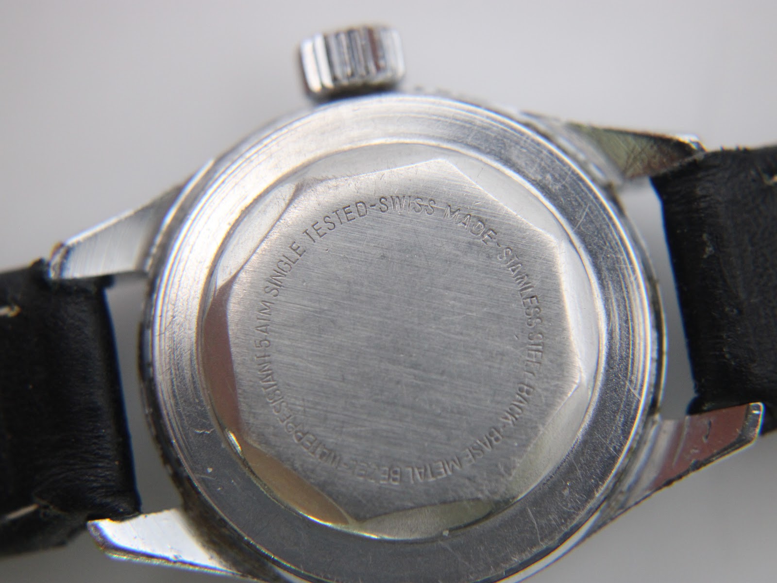 Close-up of the CASWATCH watch's stainless steel case back, with "WATER RESISTANT 5 ATM SINGLE TESTED SWISS MADE STAINLESS STEEL BACK BASE METAL BEZEL" engraving.
