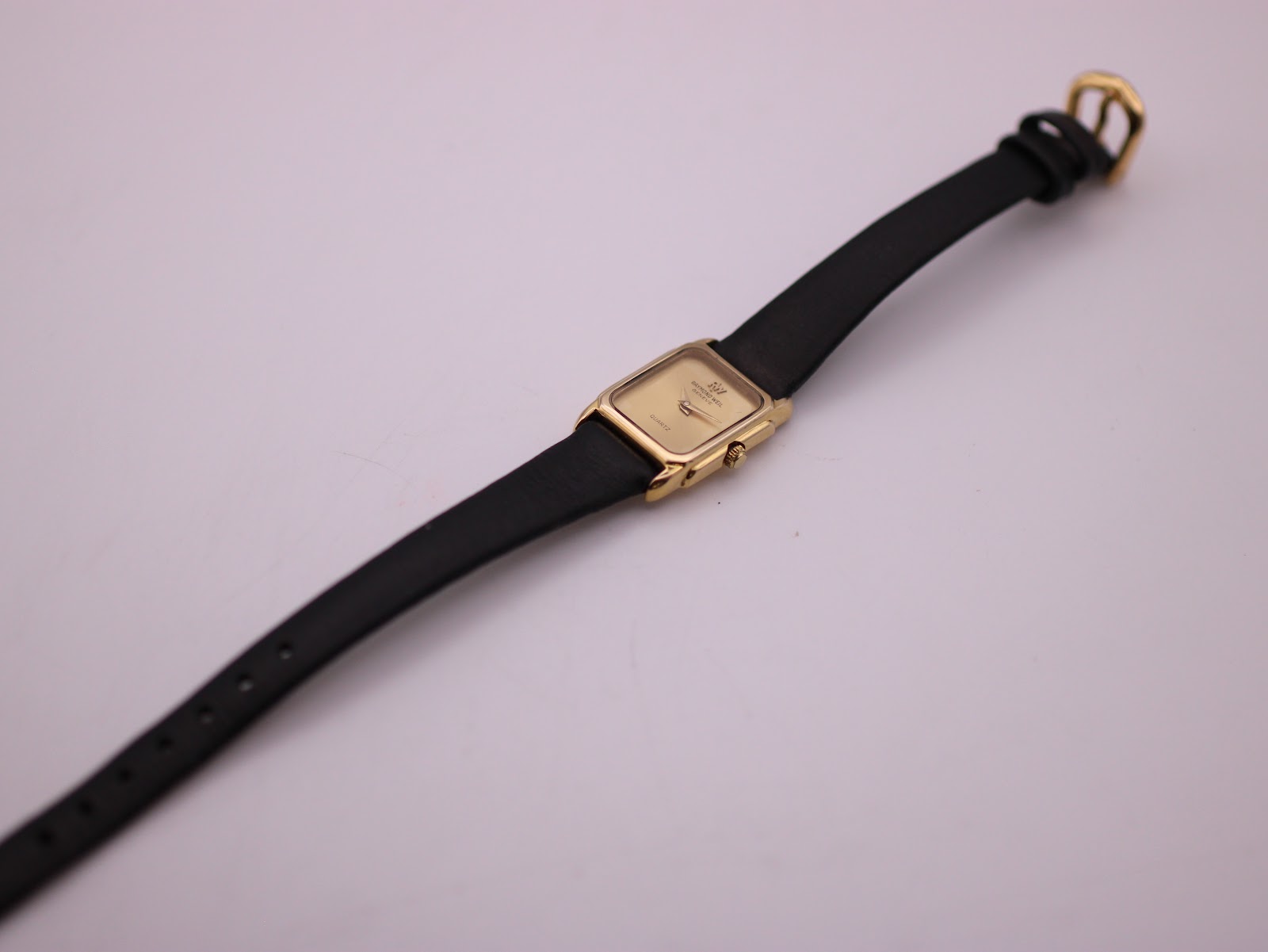 Full length view of the Raymond Weil watch with its black leather strap and gold-tone buckle on a light background.