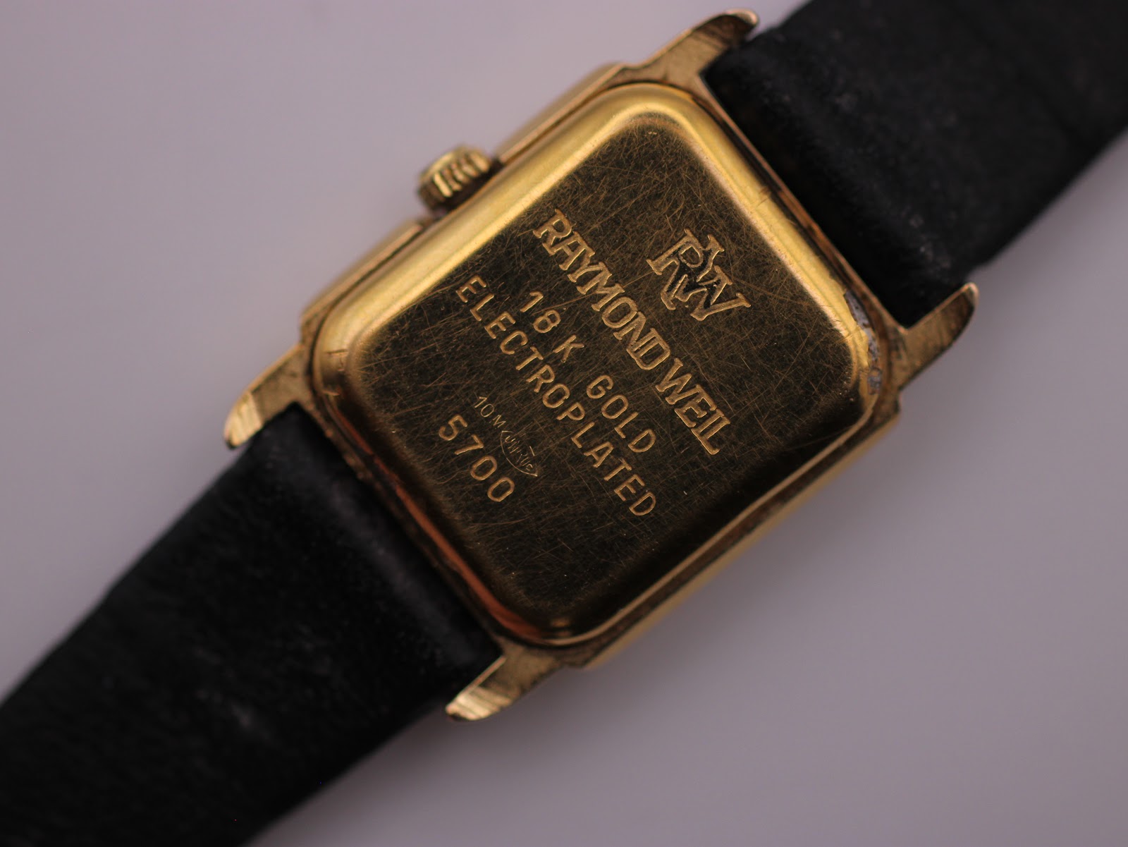 Close-up of the Raymond Weil 5700 case back, engraved with "18 K GOLD ELECTROPLATED" and "10 M QUARZ", showing light surface scratches.