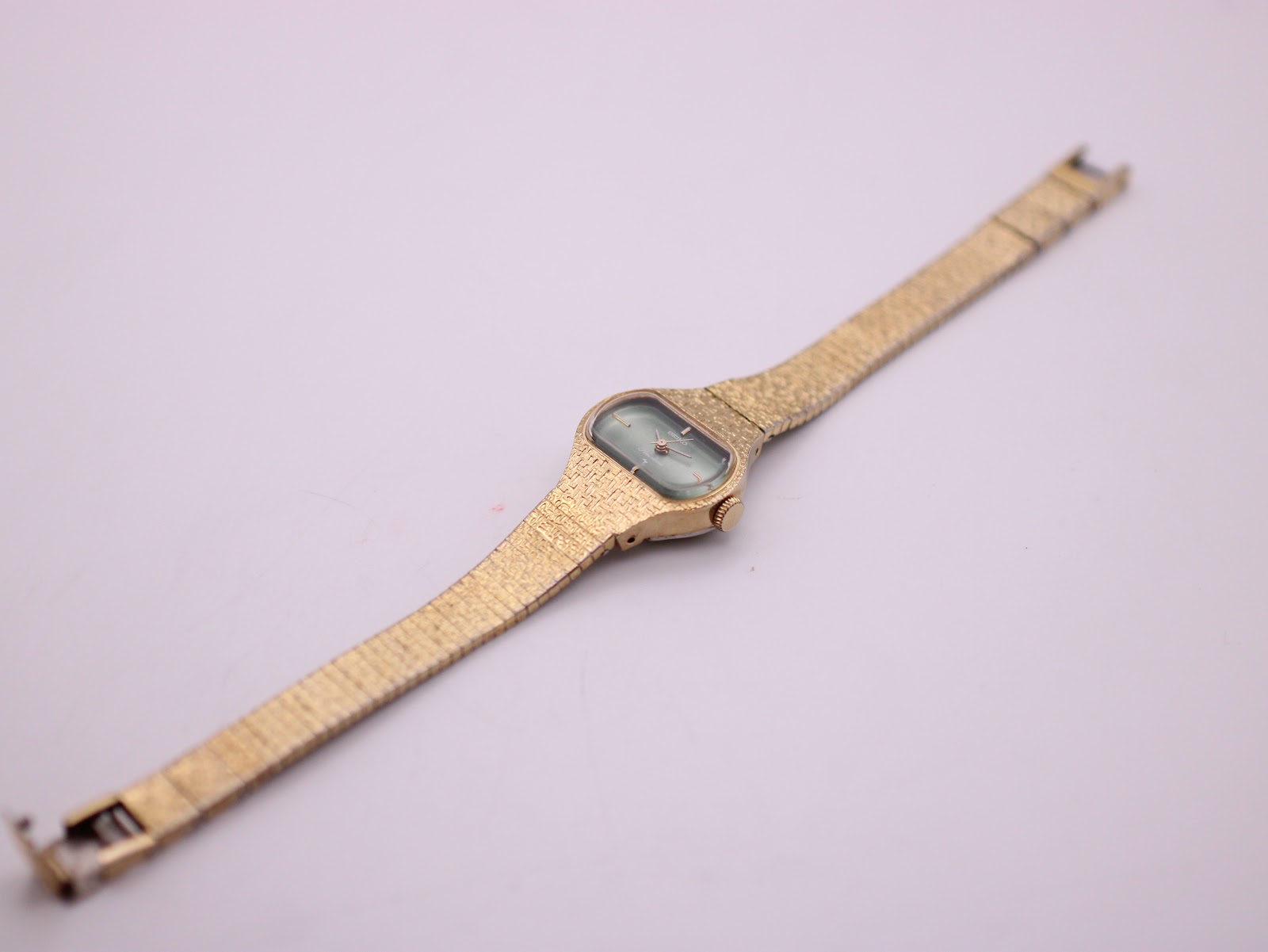 Full length overhead view of the Seiko Rainbow watch and its gold-tone textured mesh bracelet laid flat on a white background.
