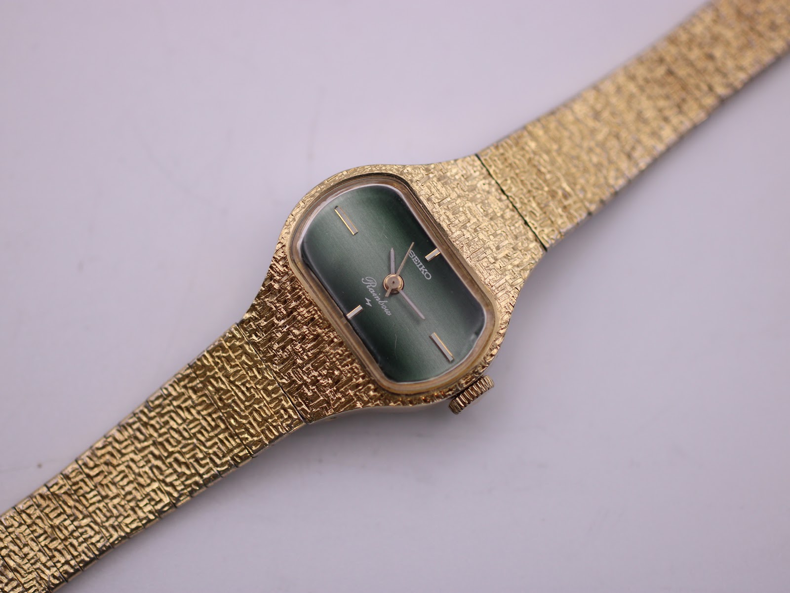 Close-up front view of the Seiko Rainbow watch, focusing on the deep green dial with gold hands and the textured gold-tone case.