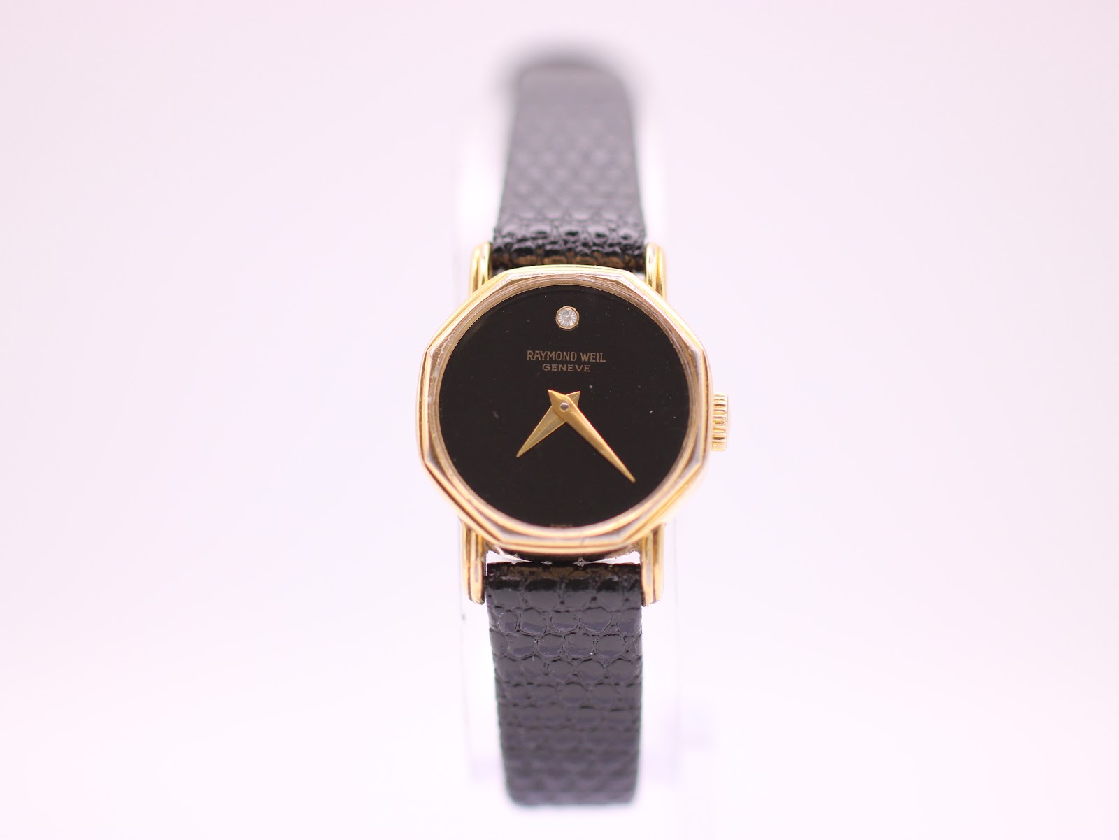 Front view of the Raymond Weil 570 watch with black dial, gold-tone octagonal case, and black leather strap.