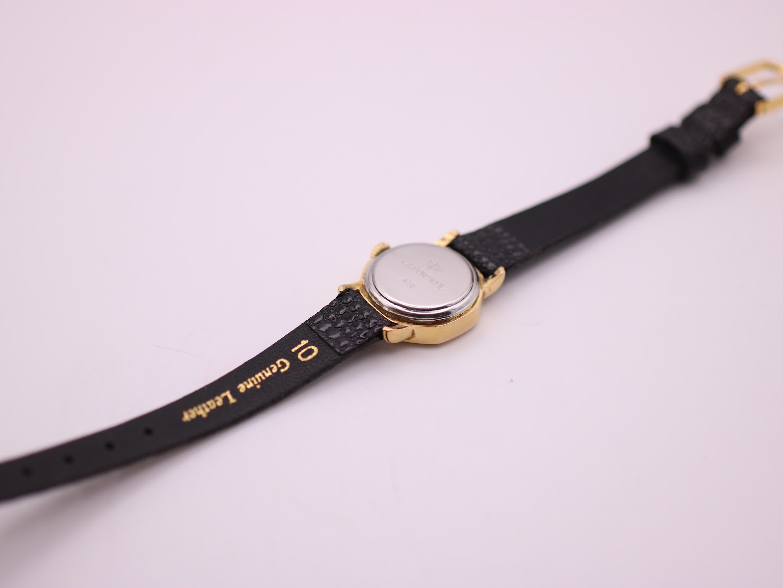 Close-up of the watch's reverse, showing the strap with "10 Genuine Leather" text and the case back.