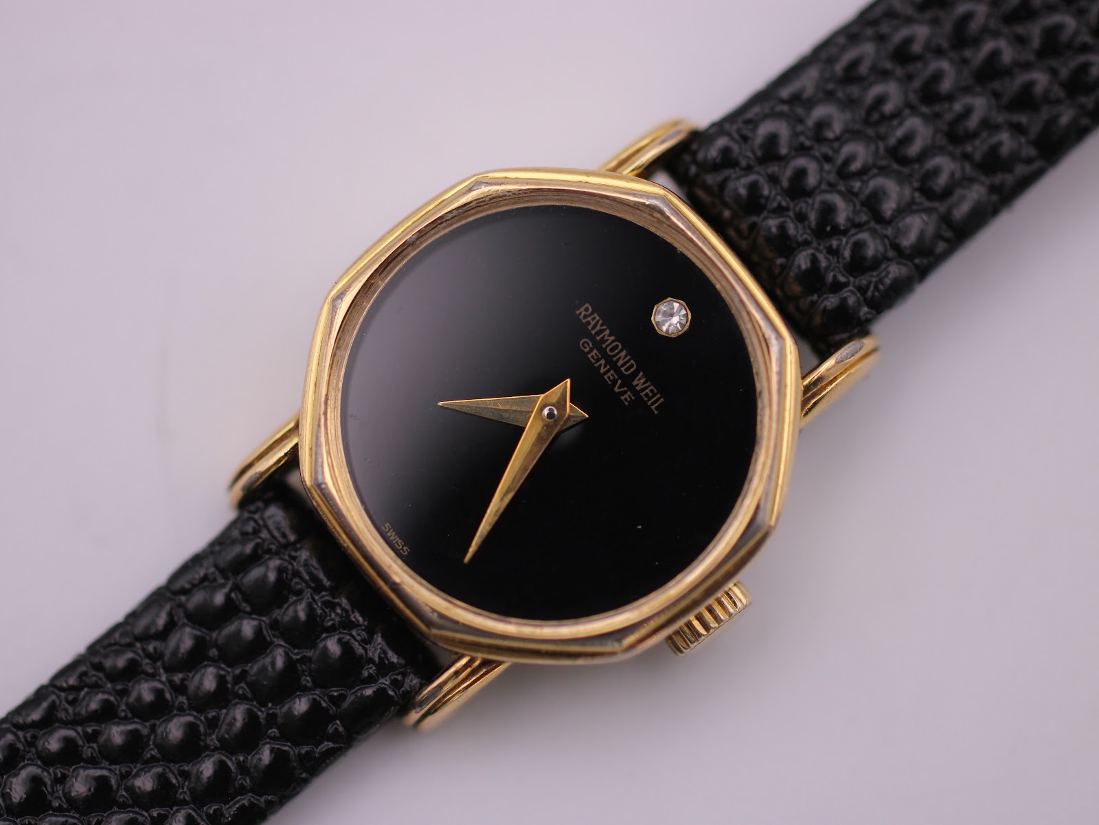 Detailed close-up of the Raymond Weil black octagonal dial, featuring gold hands and a single diamond marker at 12 o'clock.