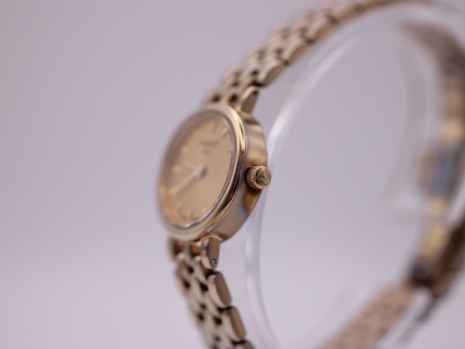 Angled side view of the Tissot watch, showing the gold-tone case, crown, and part of the bracelet.