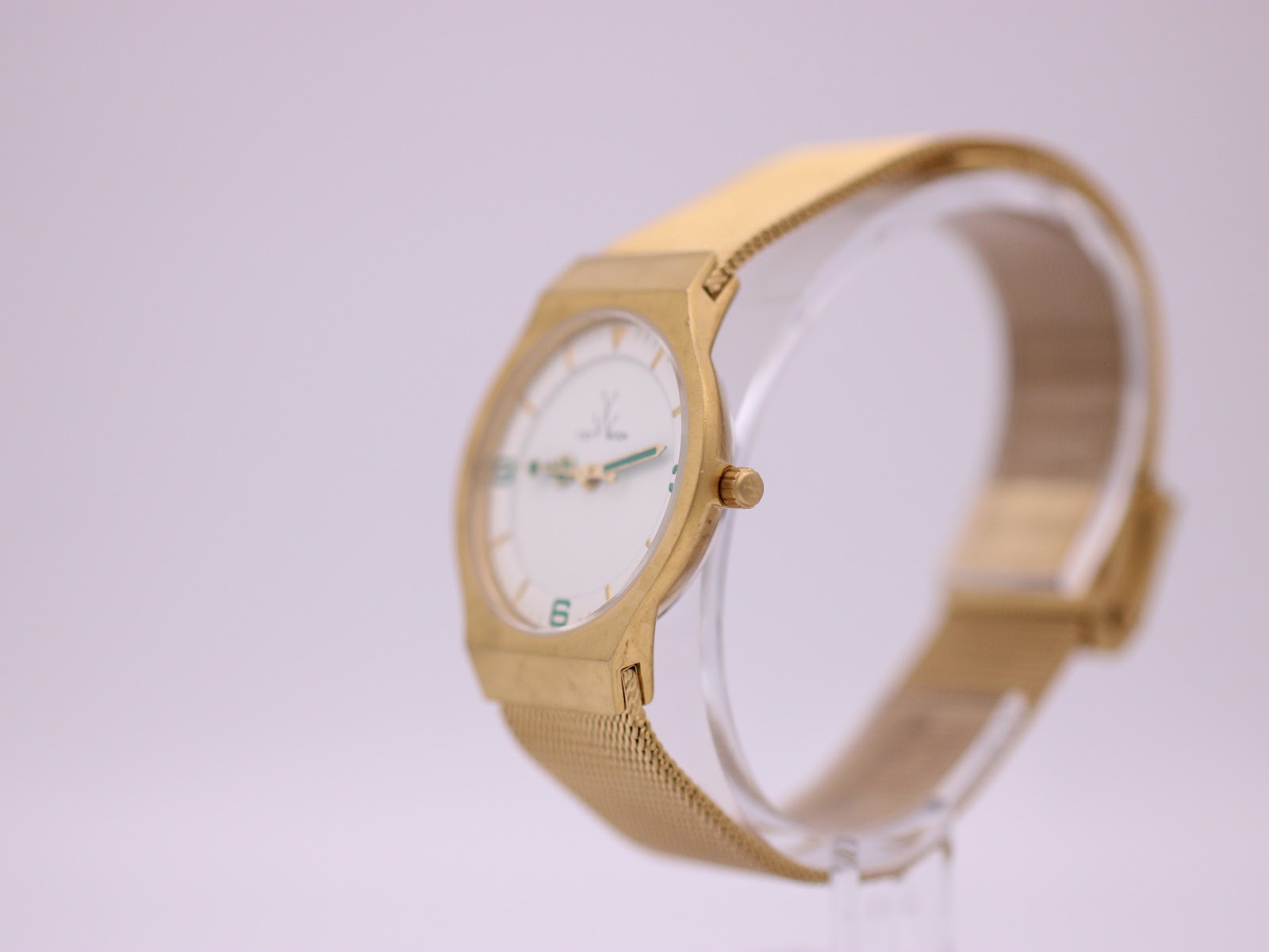 Angled side view of the Toy Watch on a clear stand, showing the case profile and mesh bracelet.