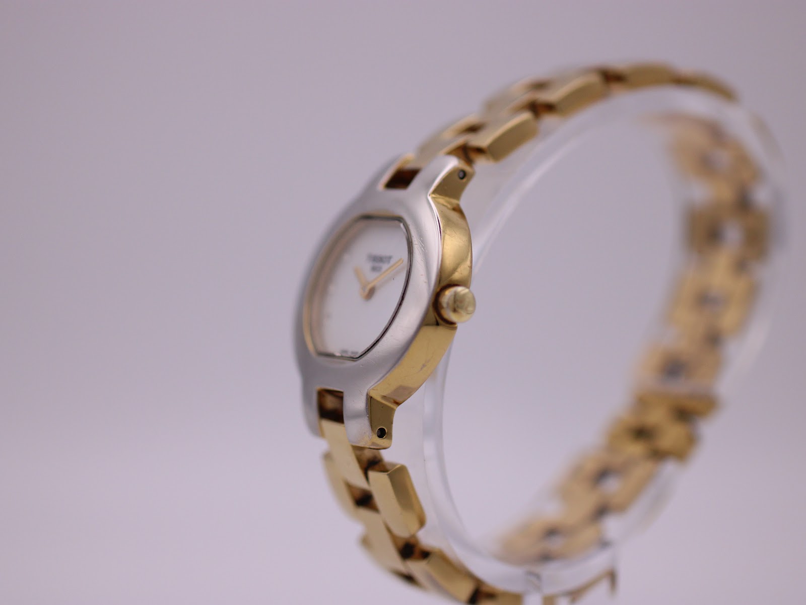 Side view of the Tissot G330 watch on a stand, showing the curved two-tone case and integrated gold-tone bracelet.