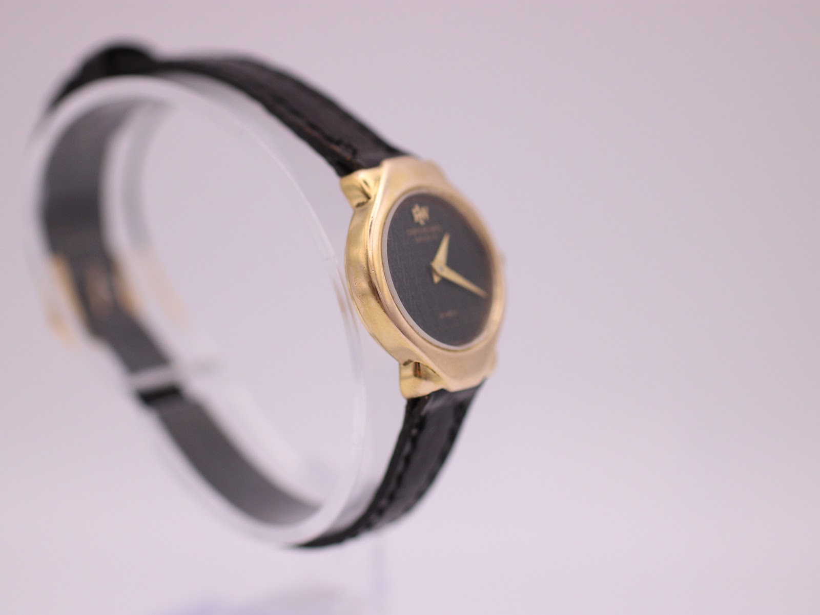 Angled view of the Raymond Weil watch showcasing the tonneau case shape, gold finish, and minimalist black dial on a stand.