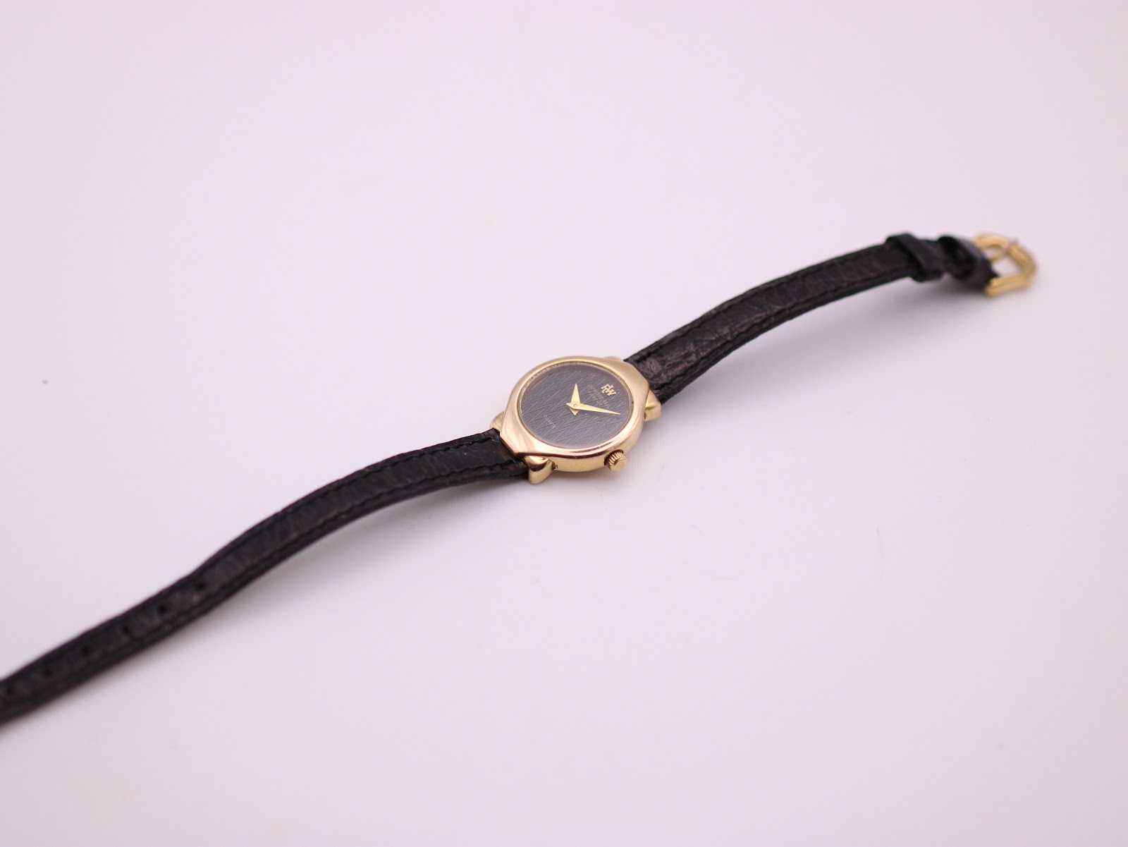 Overhead view of the entire Raymond Weil 5827 watch laid flat, highlighting the black leather strap and gold case.