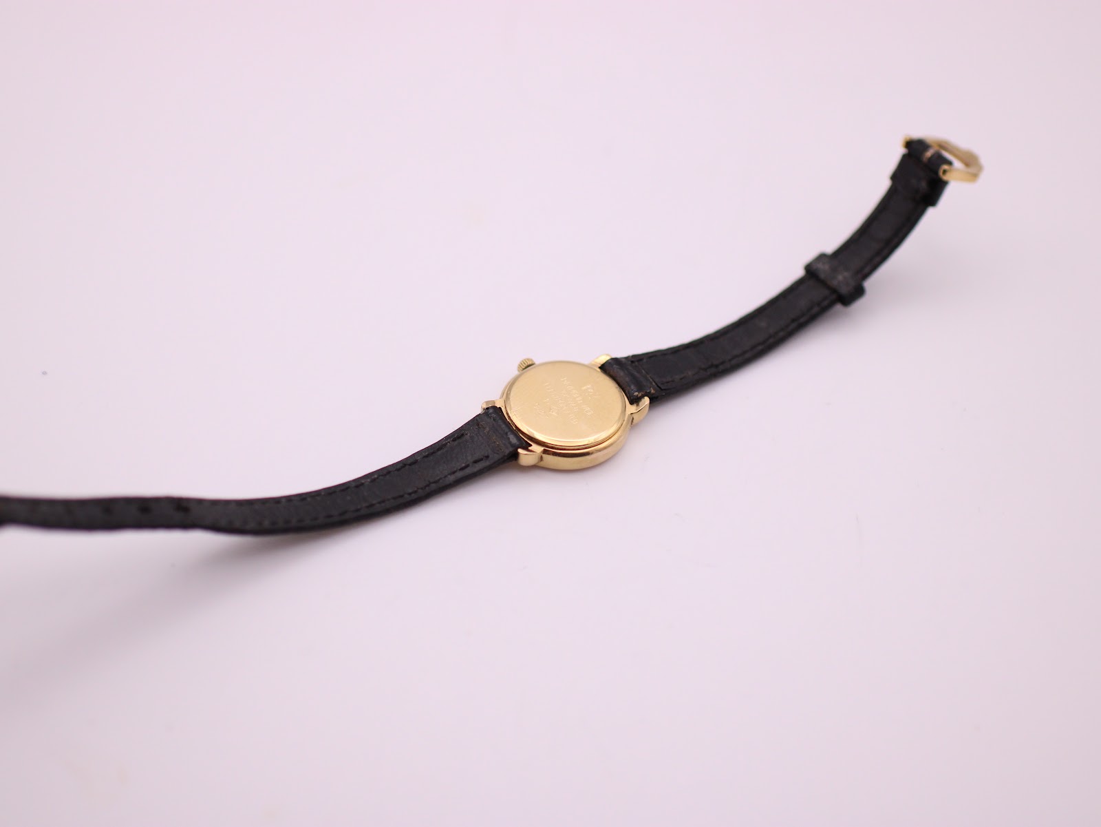 Back view of the entire Raymond Weil watch laid flat, revealing the gold case back and full length of the black leather strap.