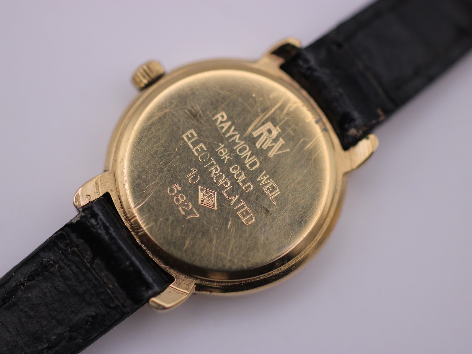 Detailed close-up of the Raymond Weil case back, clearly engraved with 'RAYMOND WEIL', '18K GOLD ELECTROPLATED', '10', and model '5827', showing surface scratches.