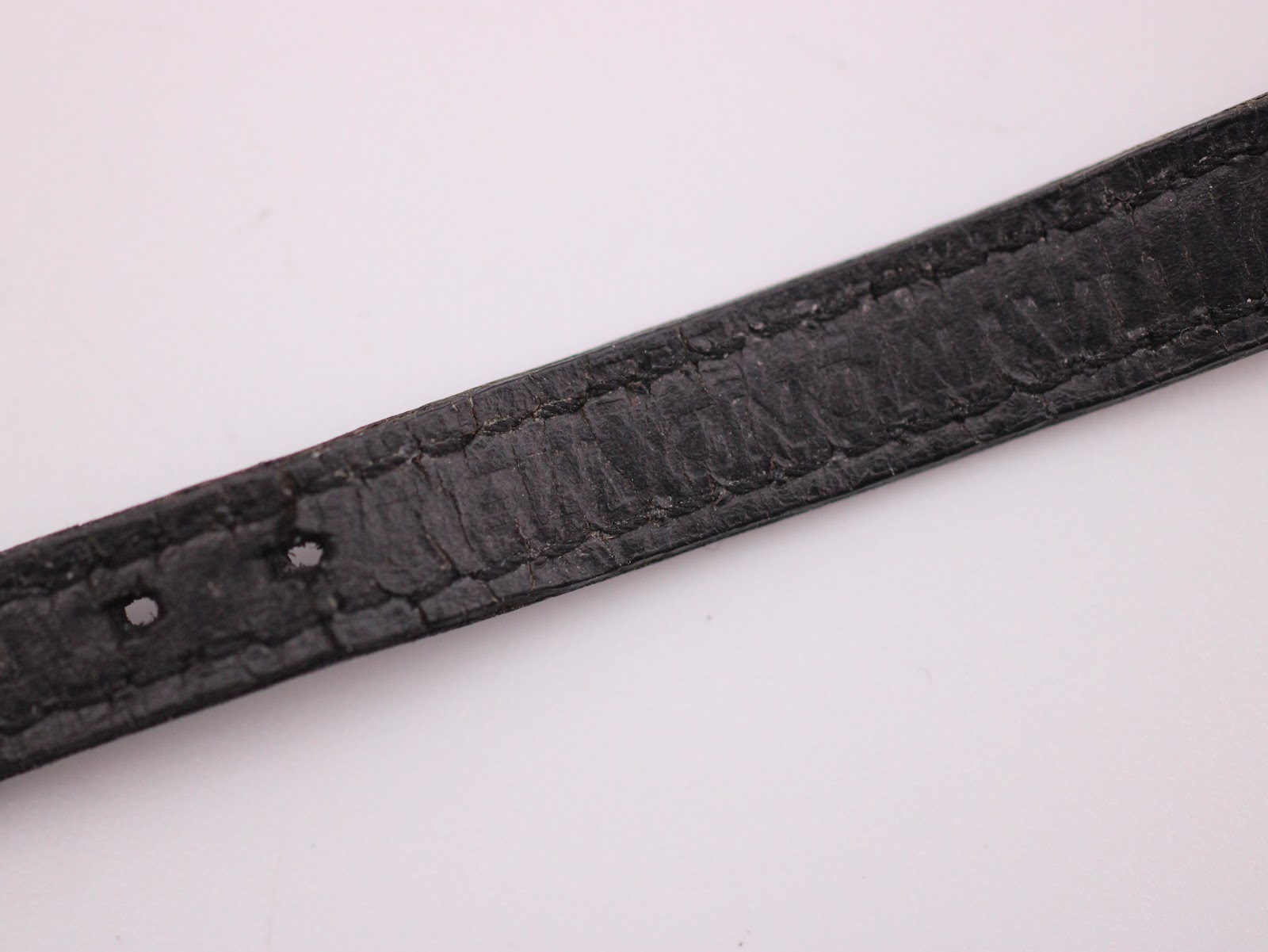 Close-up of the black leather strap, displaying its crocodile grain texture and some signs of wear and creasing.