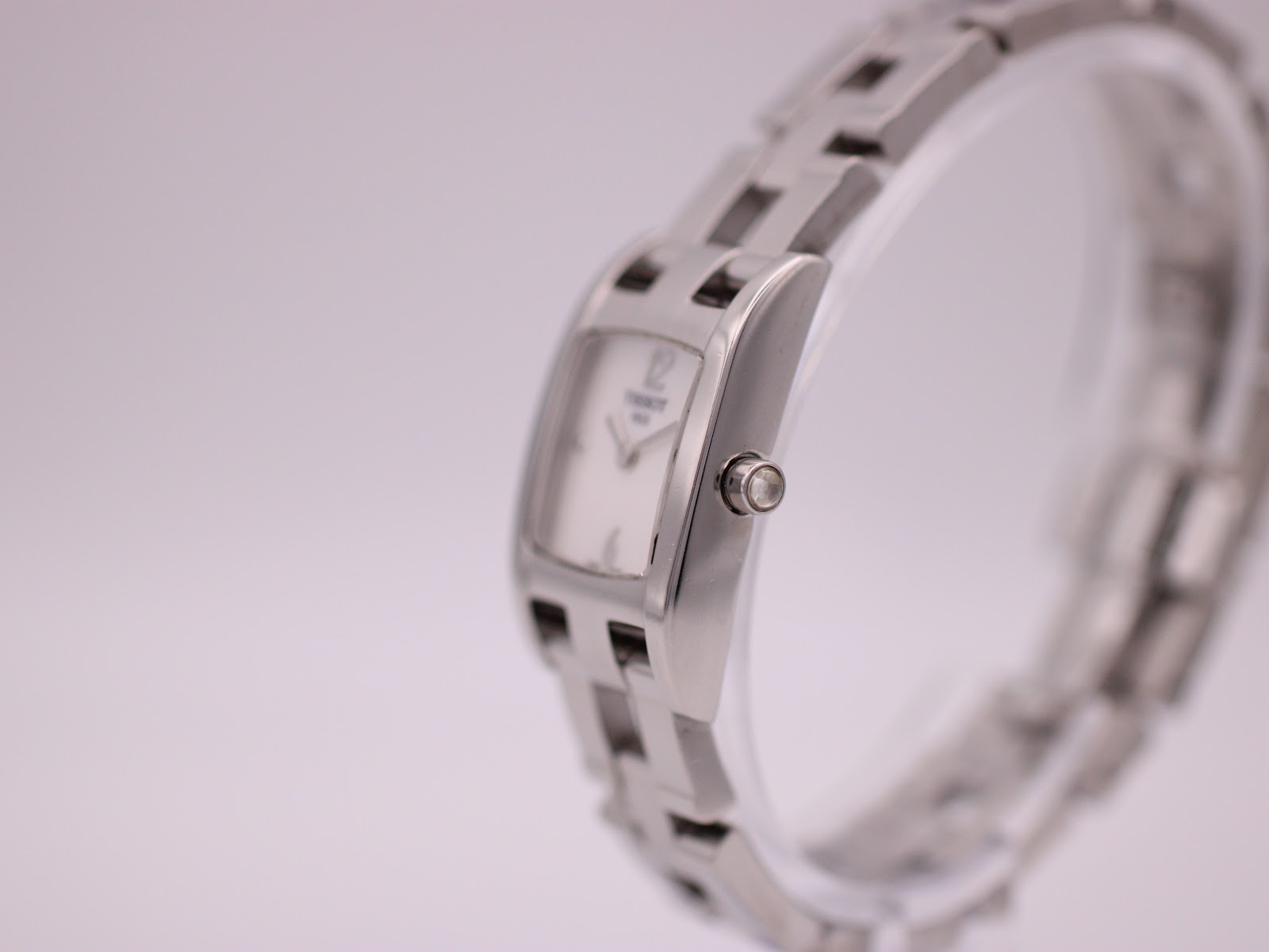 Angled side view of the Tissot watch, showing the rectangular polished case and crown detail.