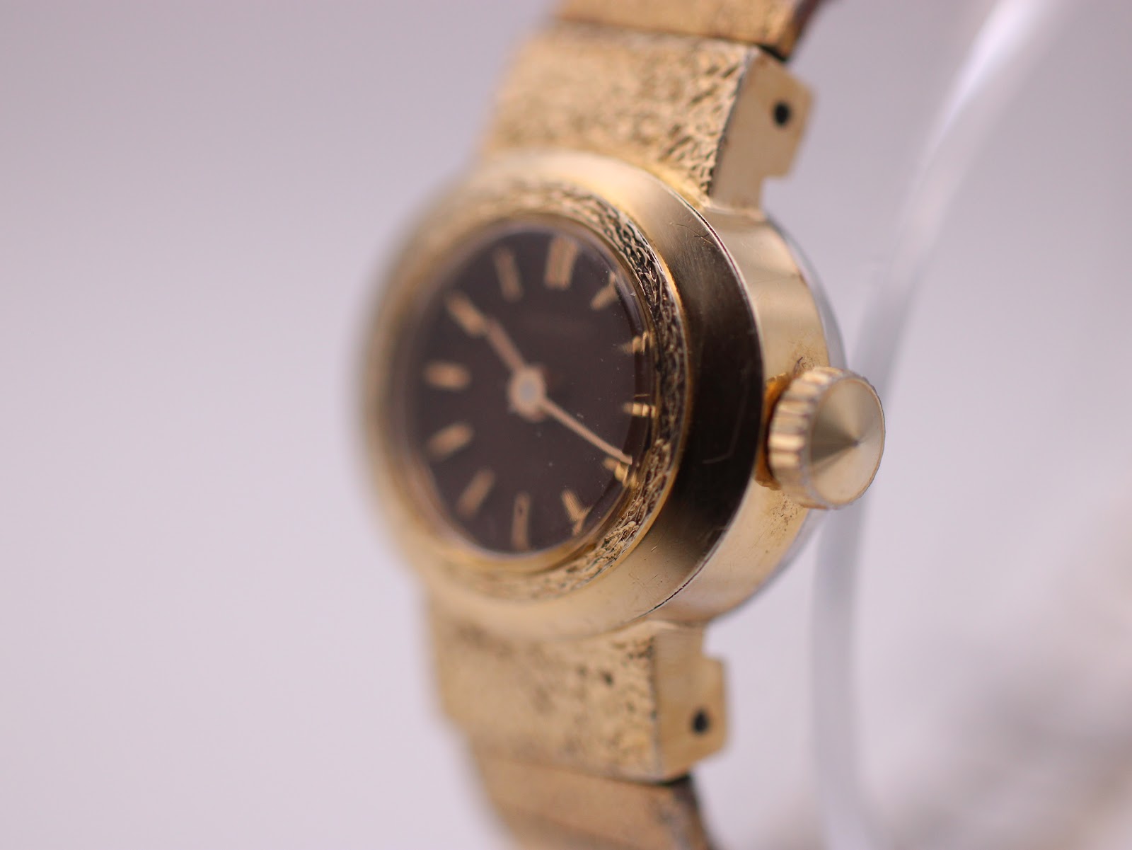 Angled close-up of the Seiko watch, showing the textured gold-plated bezel, brown dial, and crown.