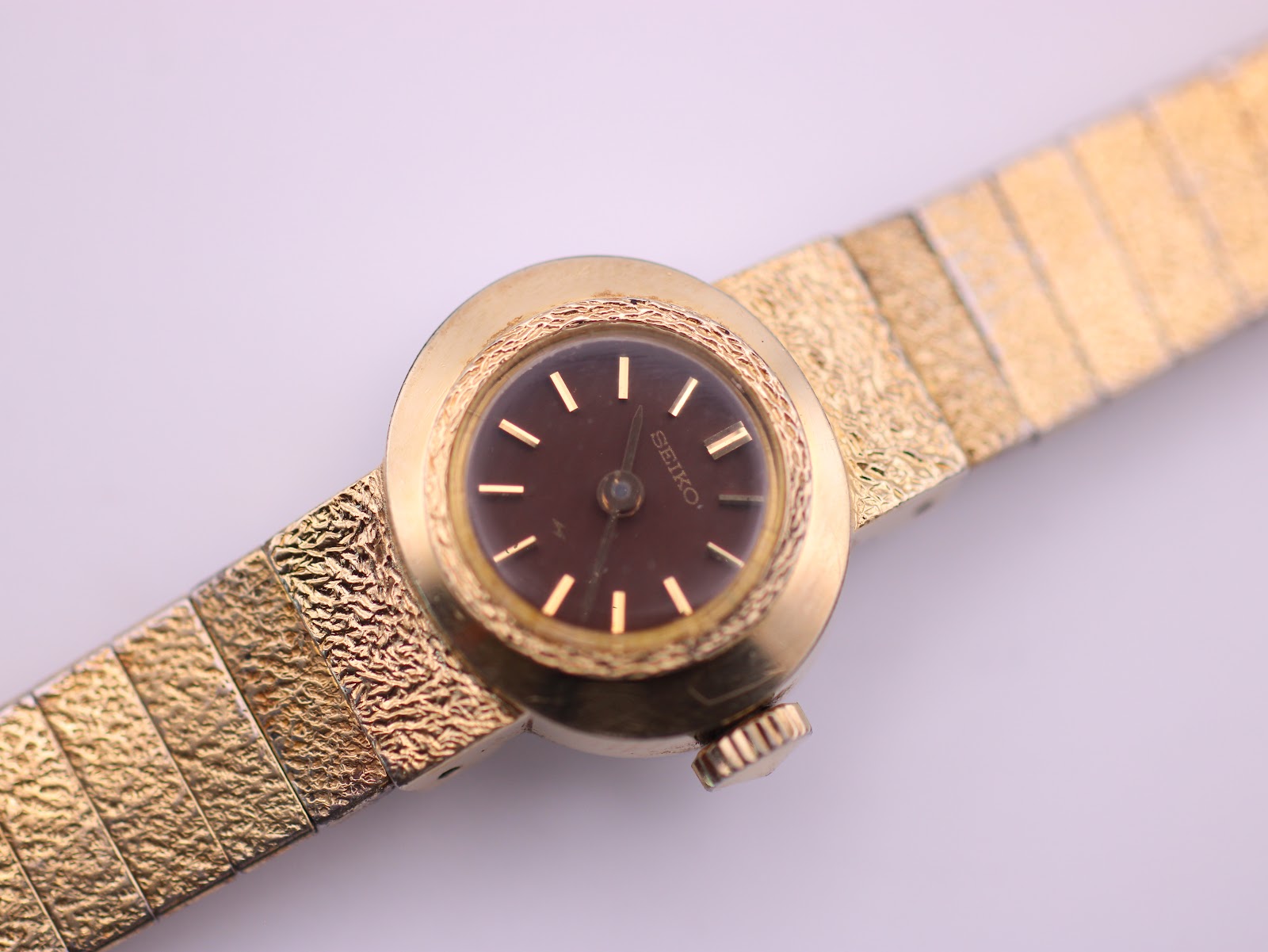 Detailed close-up of the Seiko watch dial and textured bezel, showcasing the applied gold baton indices.